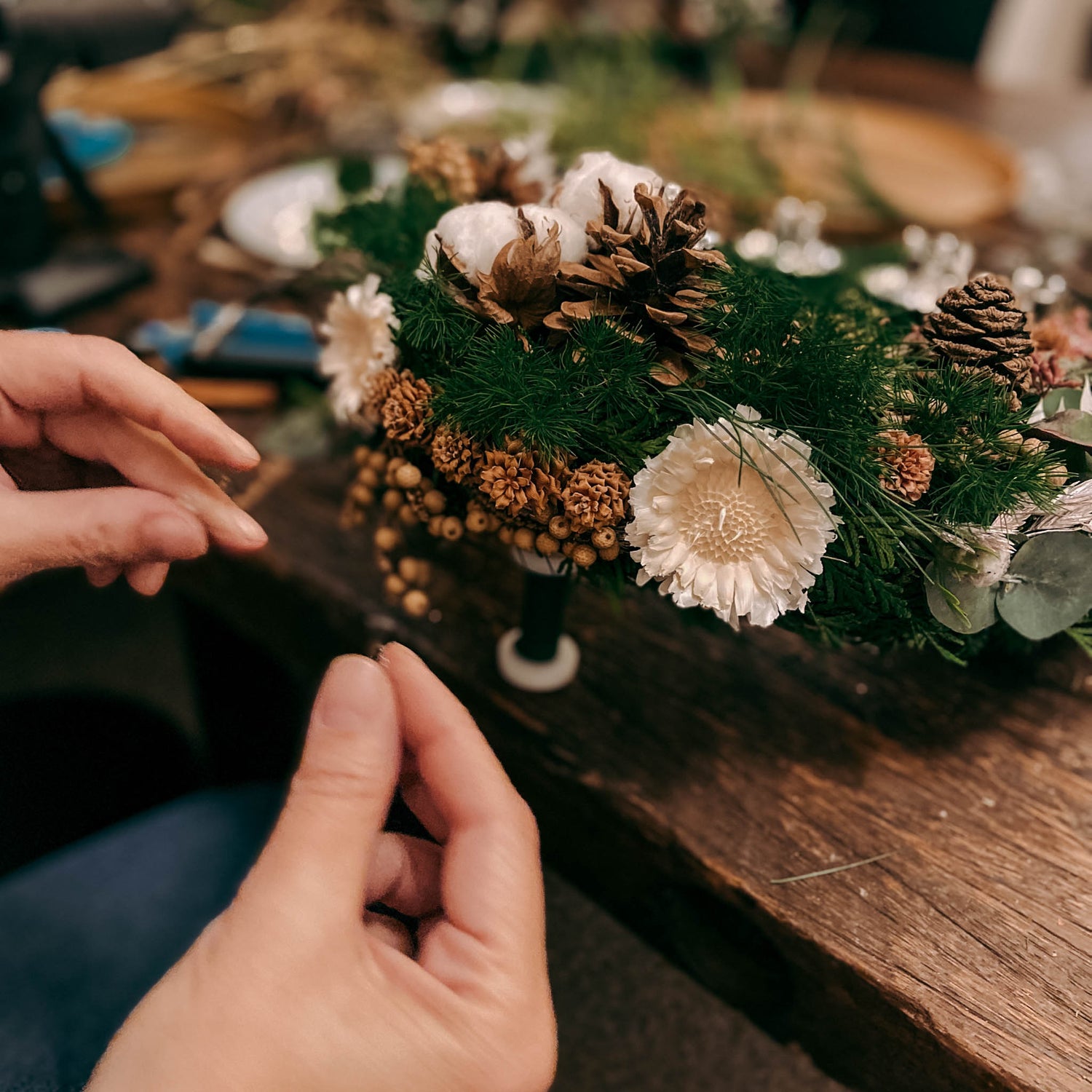 Hände befestigen Trockenblumen im grünen adventskranz – adventskranz selber machen workshop.Auch als Firmenevent buchbar.