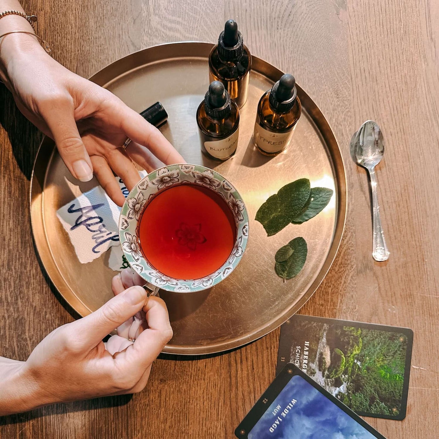 Ölmischung mit kleinen Fläschchen und Blättern auf goldenem Tablett, Hände halten Tasse – rauhnächte workshop, ätherische öle, ritual set.