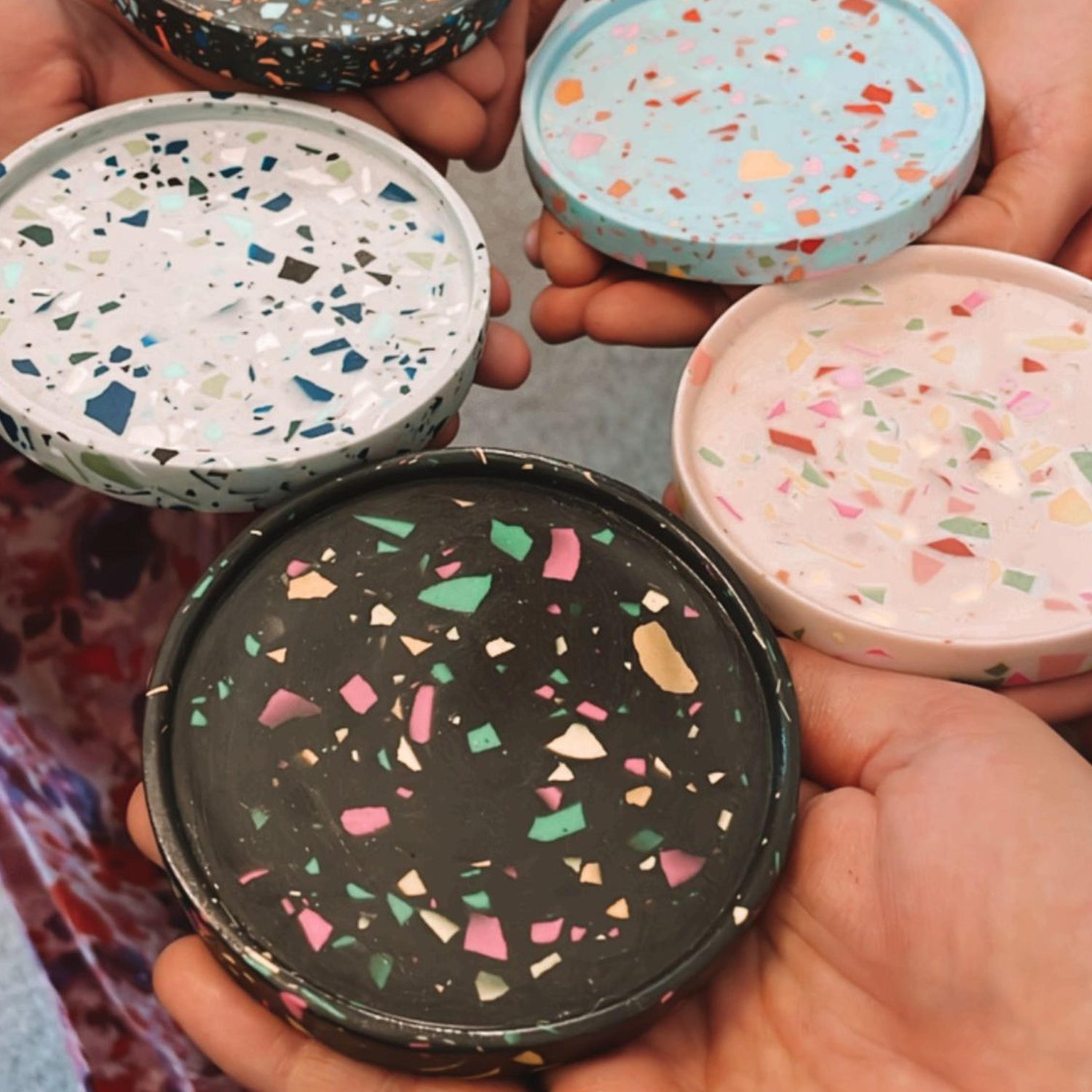 Hände zeigen Terrazzo-Untersetzer in Blau, Grau und Pink – kreativer Workshop Berlin.