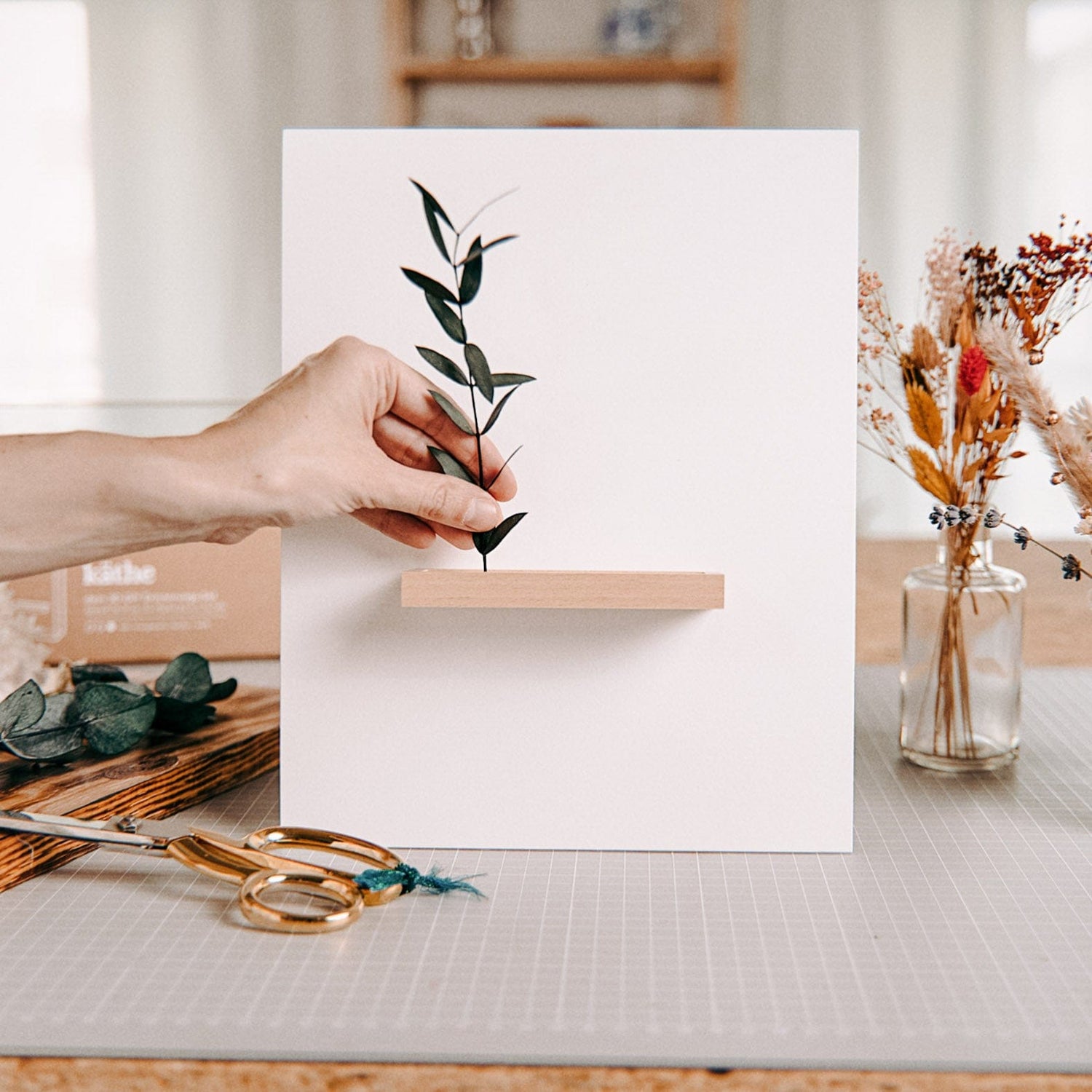 Hand steckt Eukalyptus in leeren Rahmen – trockenblumen kunstwerk workshop.