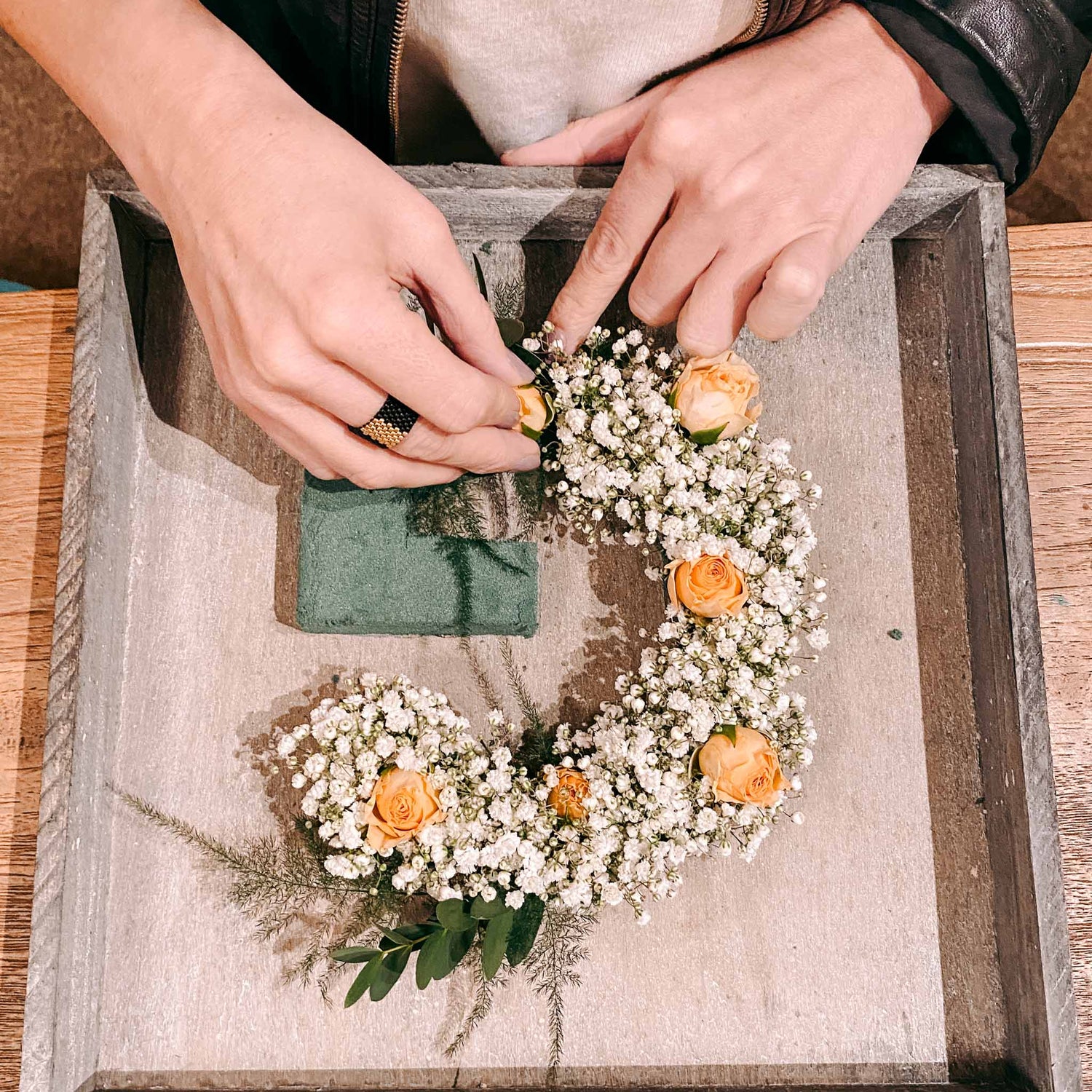Zwei Hände gestalten Blumenbuchstabe mit orangenen Blüten – blumenmonogramm selber machen, diy flower letter.