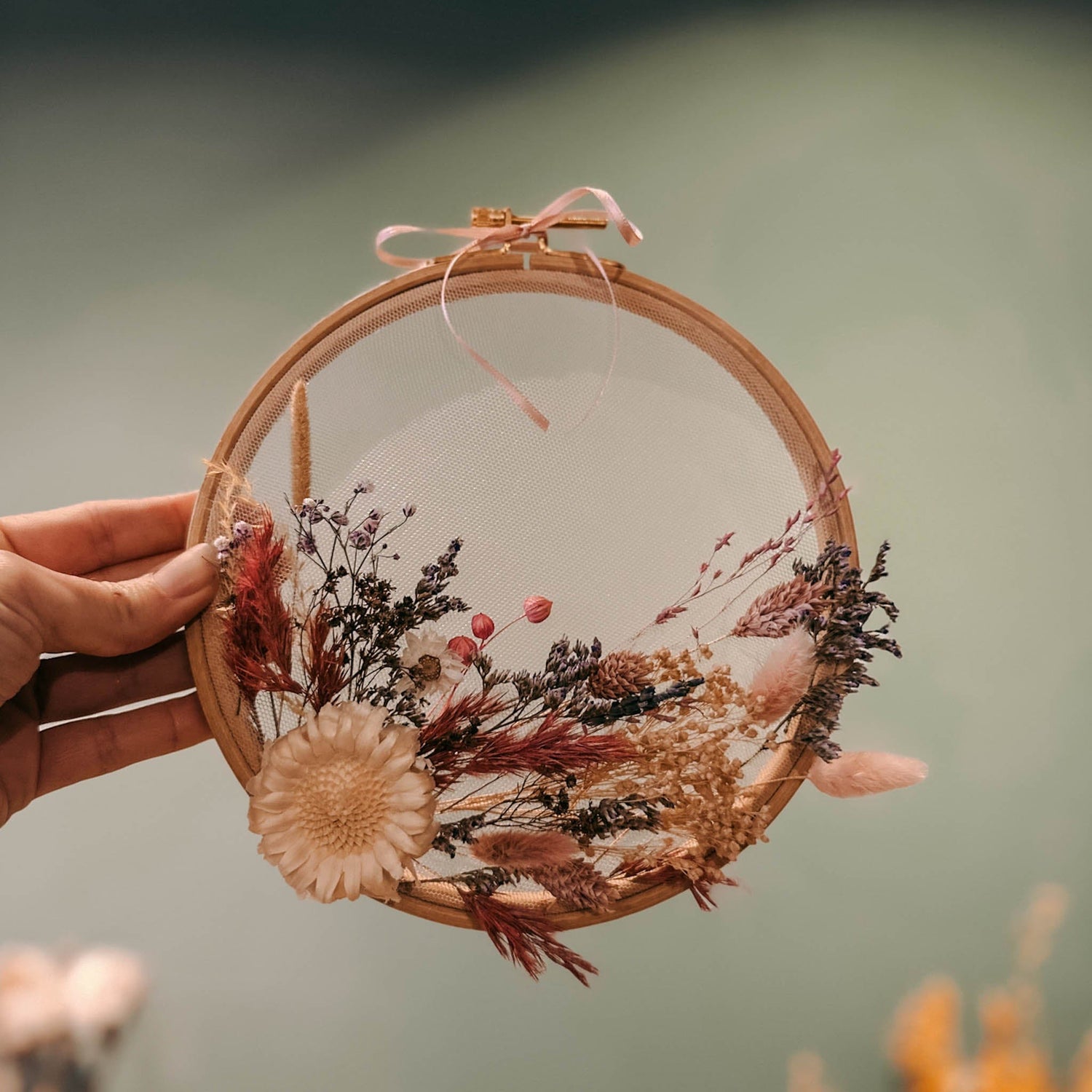 Hand hält fertiges Trockenblumenwandbild mit beigen und rosa Blumen – DIY Blumenbild, florales Kunstwerk