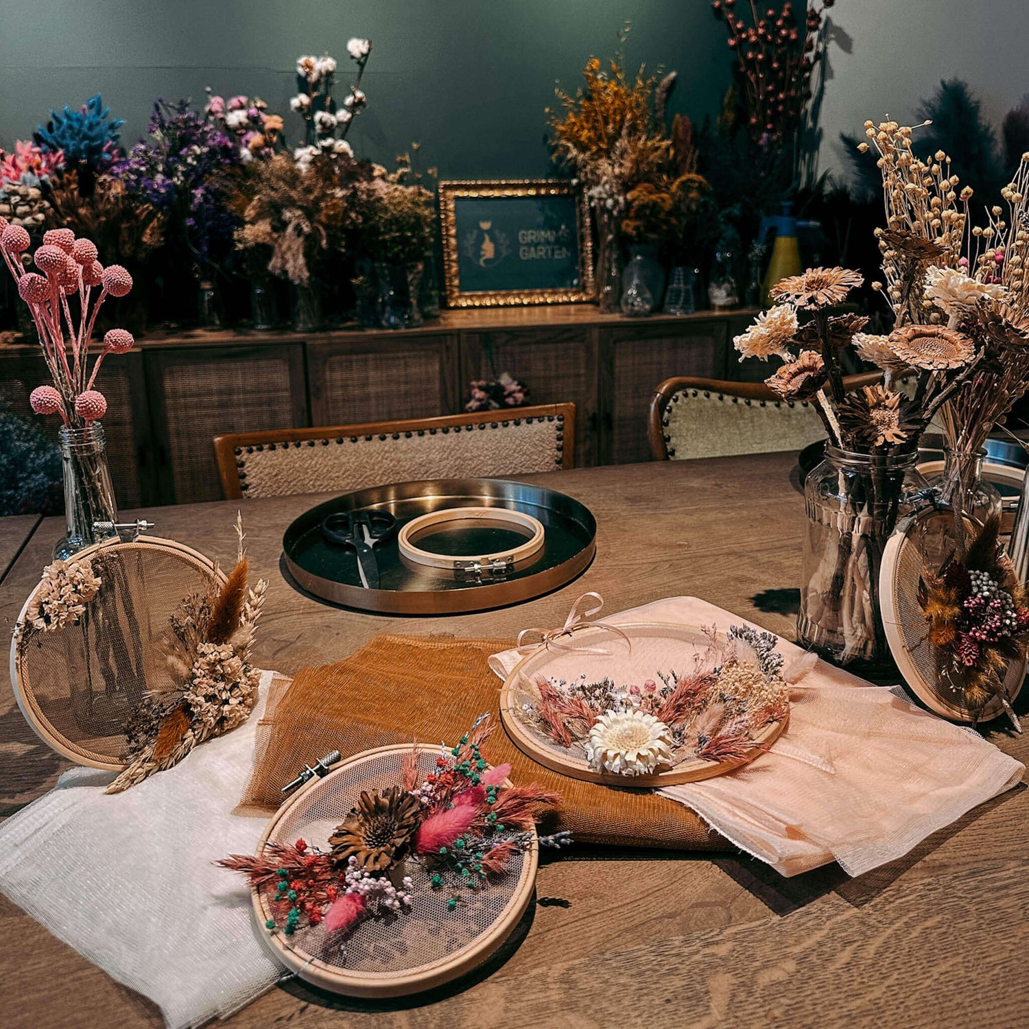 Tisch mit Trockenblumen in Vasen und vielen fertigen Wandbildern in Farben und Formen – DIY Blumenbild, florales Kunstwerk