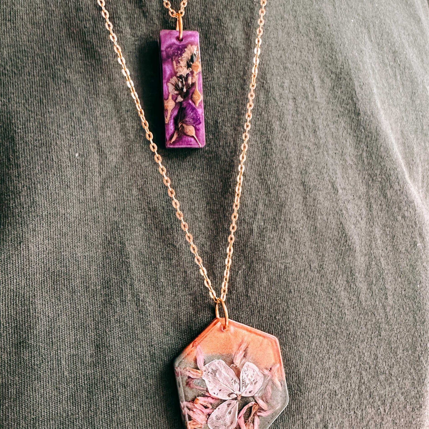 Zwei farbige Resin-Anhänger mit echten Blumen an Ketten, Nahaufnahme aus kreativem Workshop bei Grimms Garten Berlin