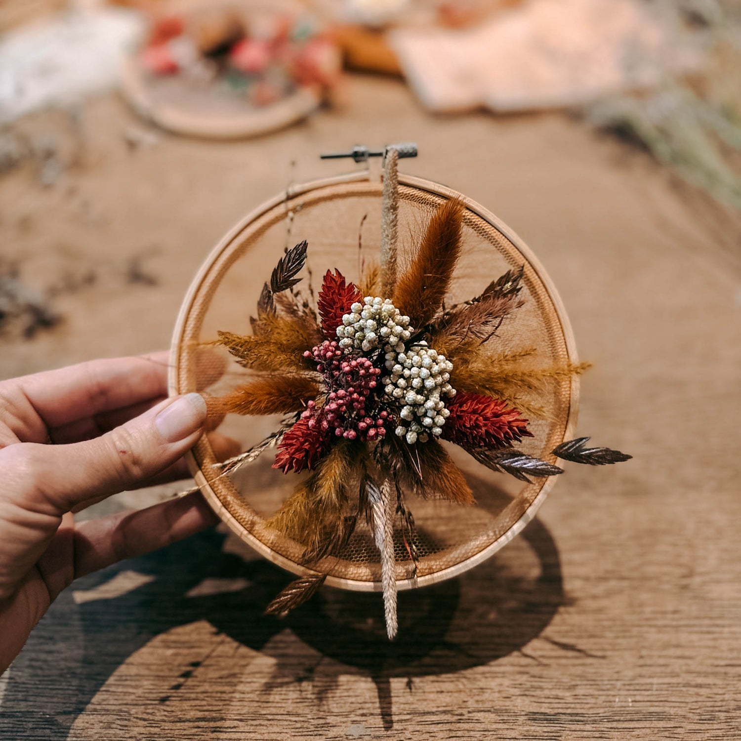 Hand hält fertigen Trockenblumenring mit orangenen, roten und rosa Blumen – DIY Trockenblumenring, Blumenrahmen selber machen