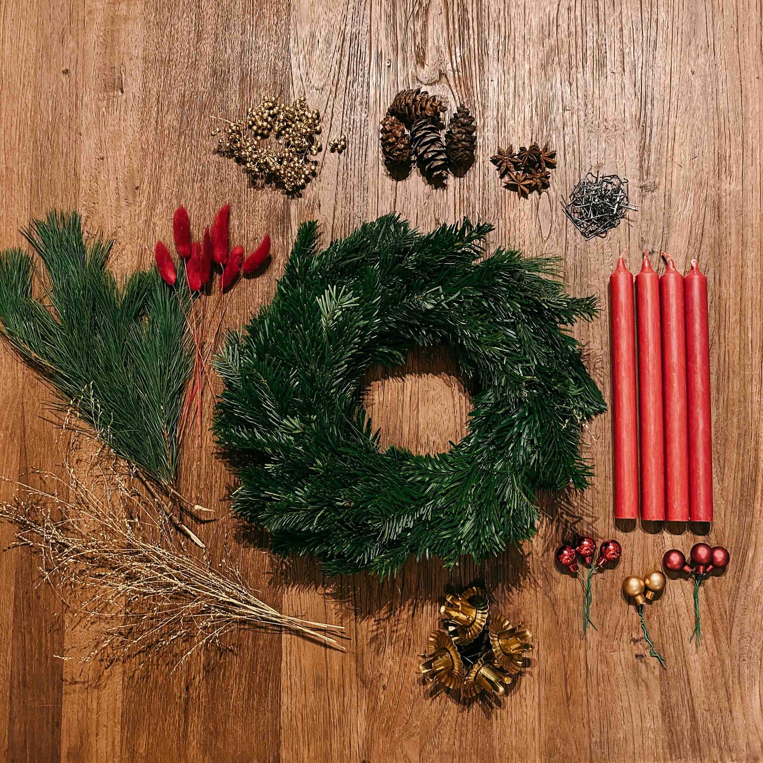 Holztisch mit Tannenzweigen, roten Kerzen und Kugeln – Materialien aus Adventskranz DIY Box Rotkäppchen.