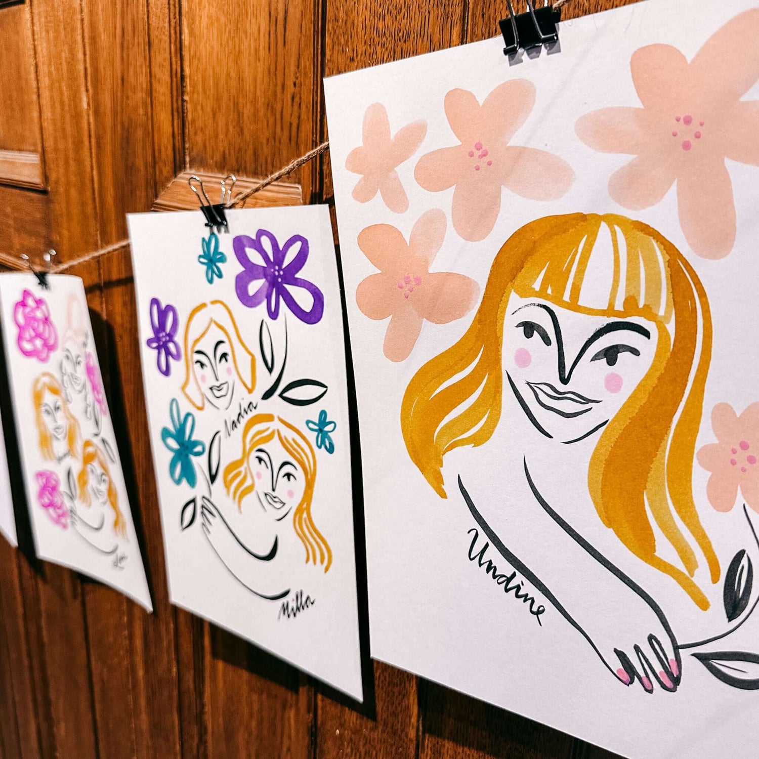 Drei fertige Aquarell-Portraits hängen an Schnur mit bunten Blumen – kreative Teamevent Dekoration.