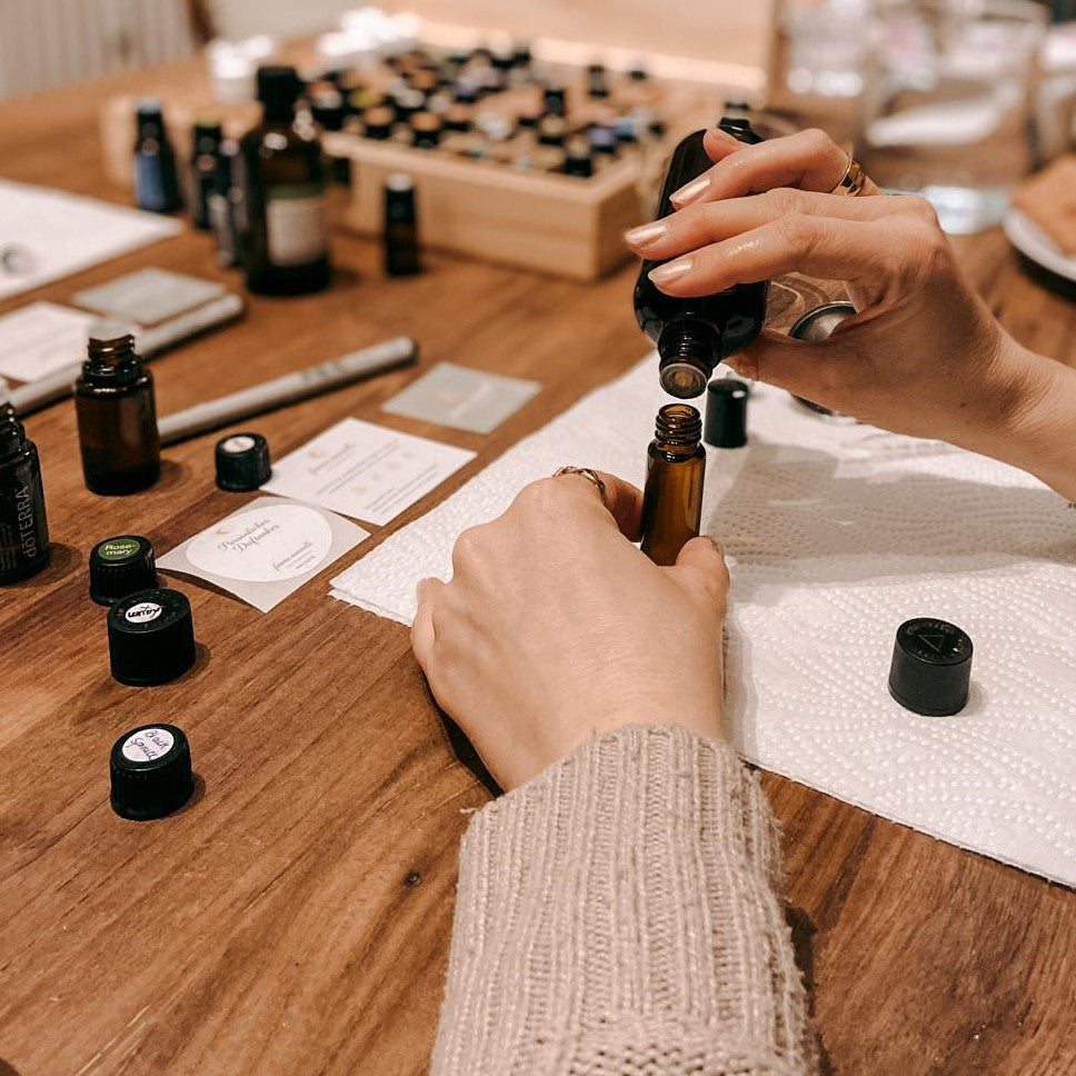Zwei Hände befüllen kleine Flasche mit Öl, Materialien im Hintergrund – parfum workshop, ätherische öle, naturkosmetik, auch für Firmenevents.