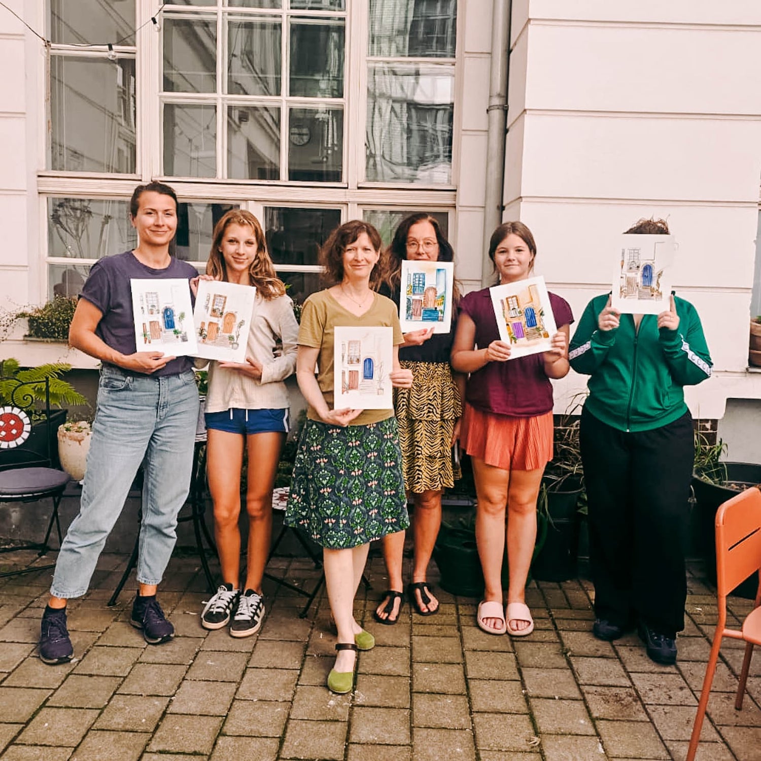 Gruppe hält fertige Aquarellbilder beim kreativen Teamevent und Aquarell Workshop von GRIMMS GARTEN Berlin in die Höhe