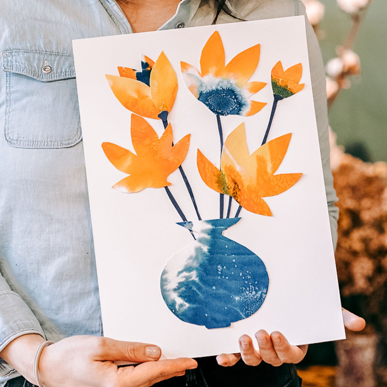 Person zeigt fertiges Bouquet mit blauer Vase und orangenen Blumen – Aquarell Workshop für Flower-Art.