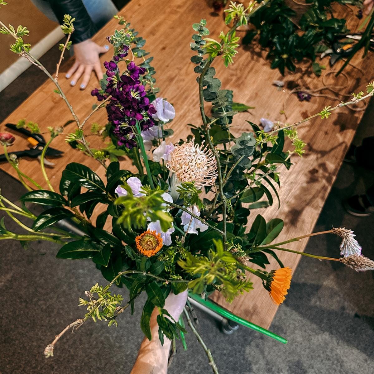 Nahaufnahme Blumenstrauß mit lila und orangenen Blumen in Hand – Workshop für Teams oder Einzelpersonen.
