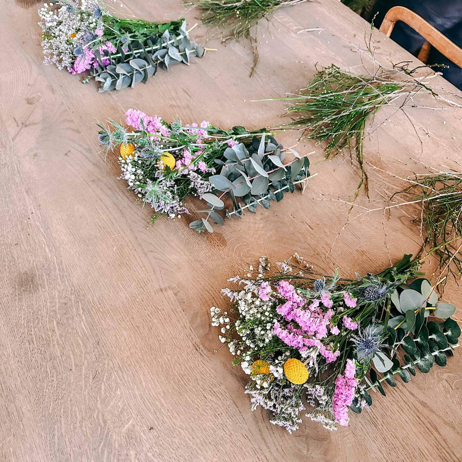 Drei Blumensträuße mit grünen Zweigen auf Tisch – Vorbereitung für DIY Frühlingskranz.