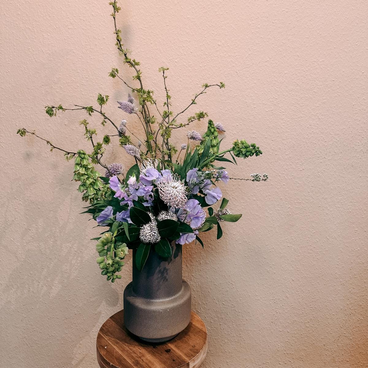 Blumenstrauß mit lila Akzenten in Vase auf Holzhocker – DIY Flower Bouquet Workshop, Team-Option verfügbar.