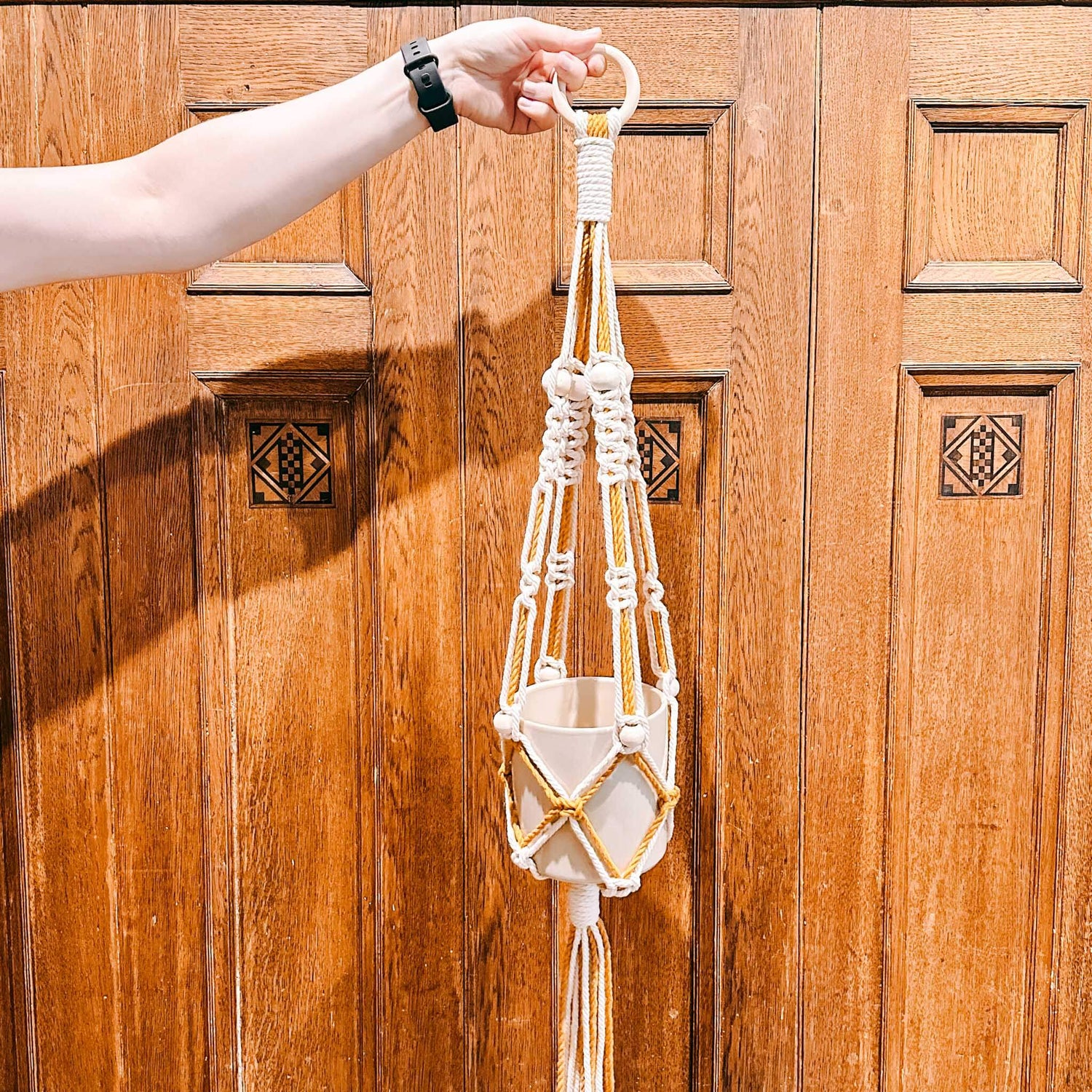 Hand hält Makramee-Blumenampel mit leerem Blumentopf – DIY Makramee, Blumenampel knoten, Boho Style.