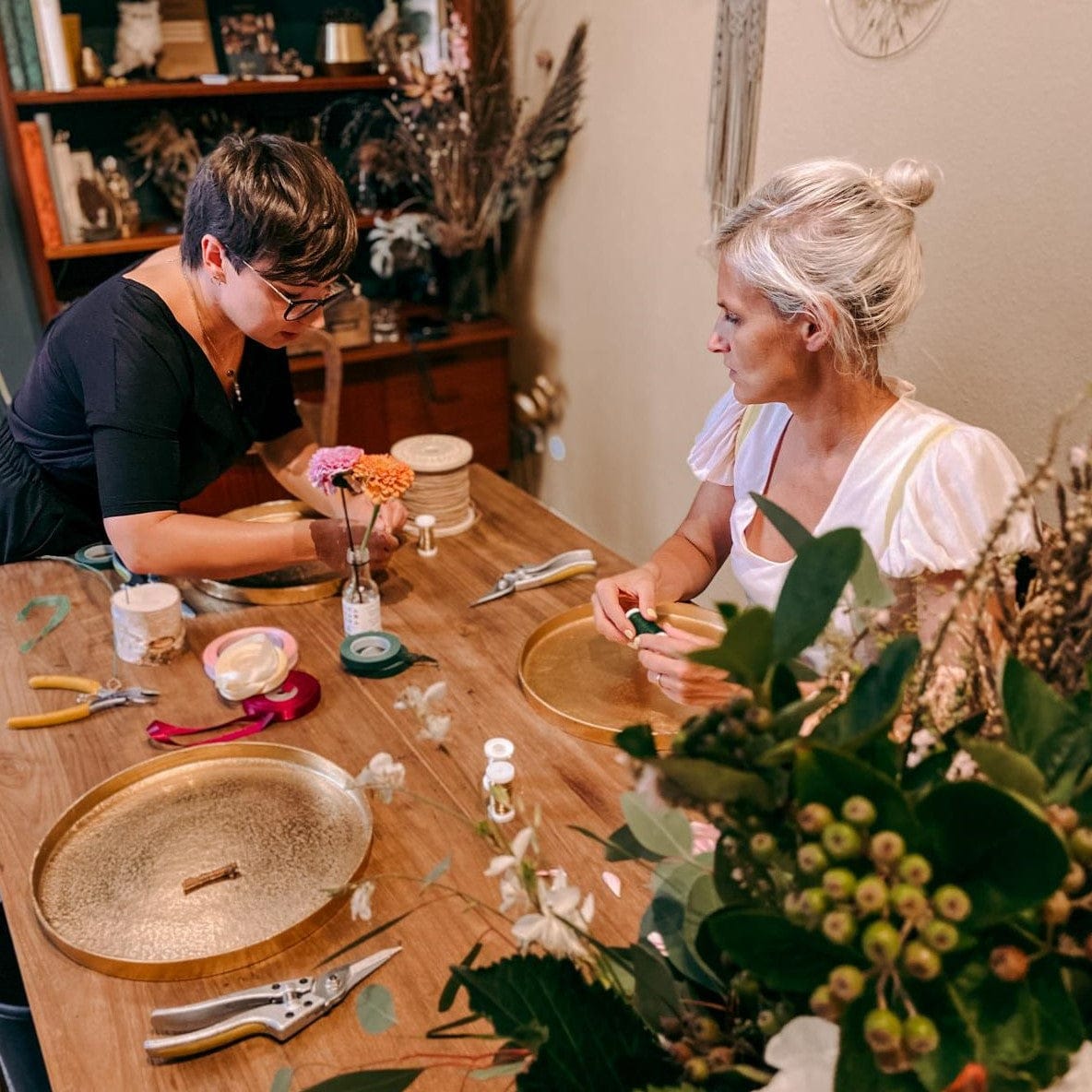 Zwei Frauen basteln Blumenkranz an Holztisch, kreativer DIY Workshop bei Grimms Garten Berlin