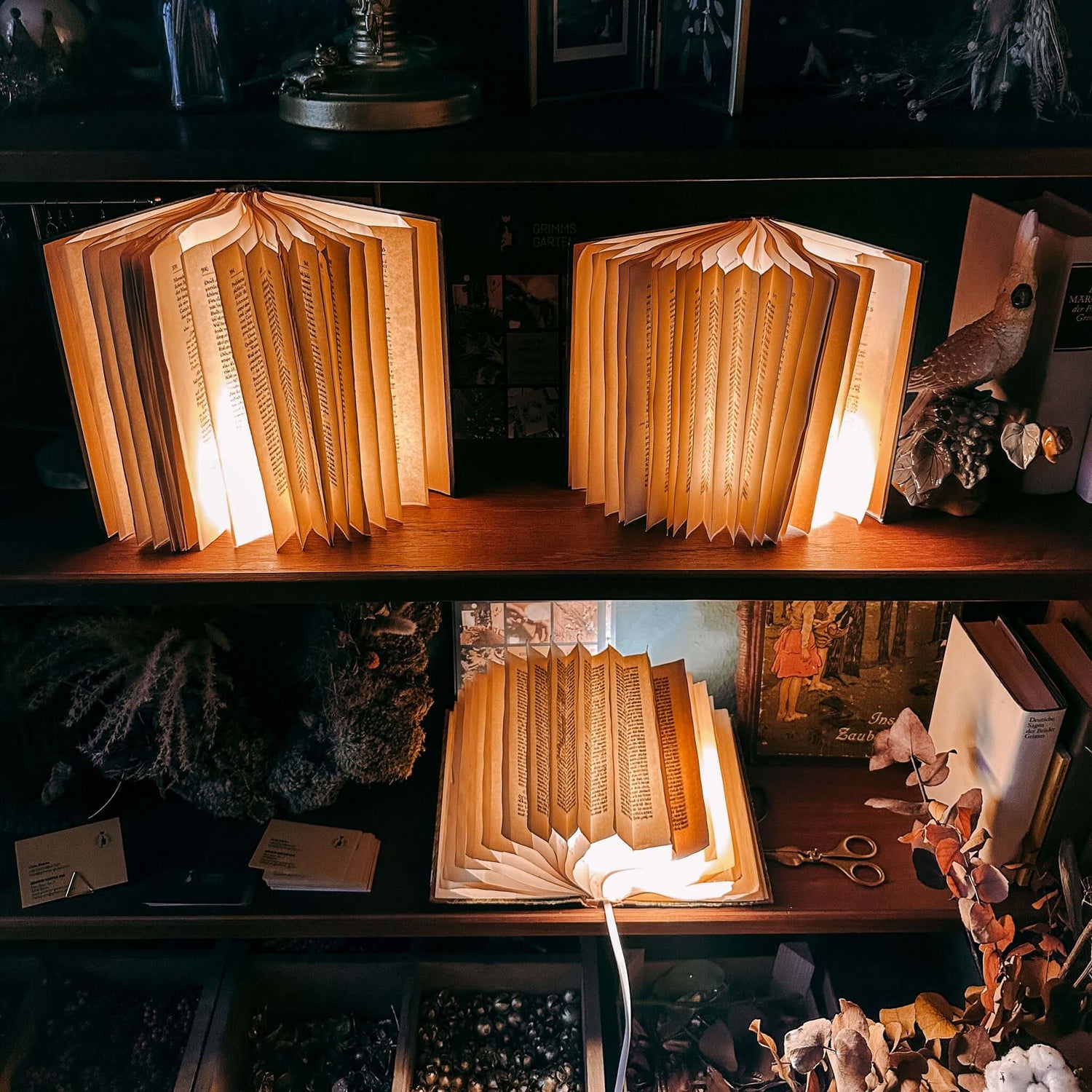 Drei leuchtende Buchlampen im Regal mit Dekoration – upcycling lampen, nachhaltiges design, diy deko. Auch für Firmenevents.