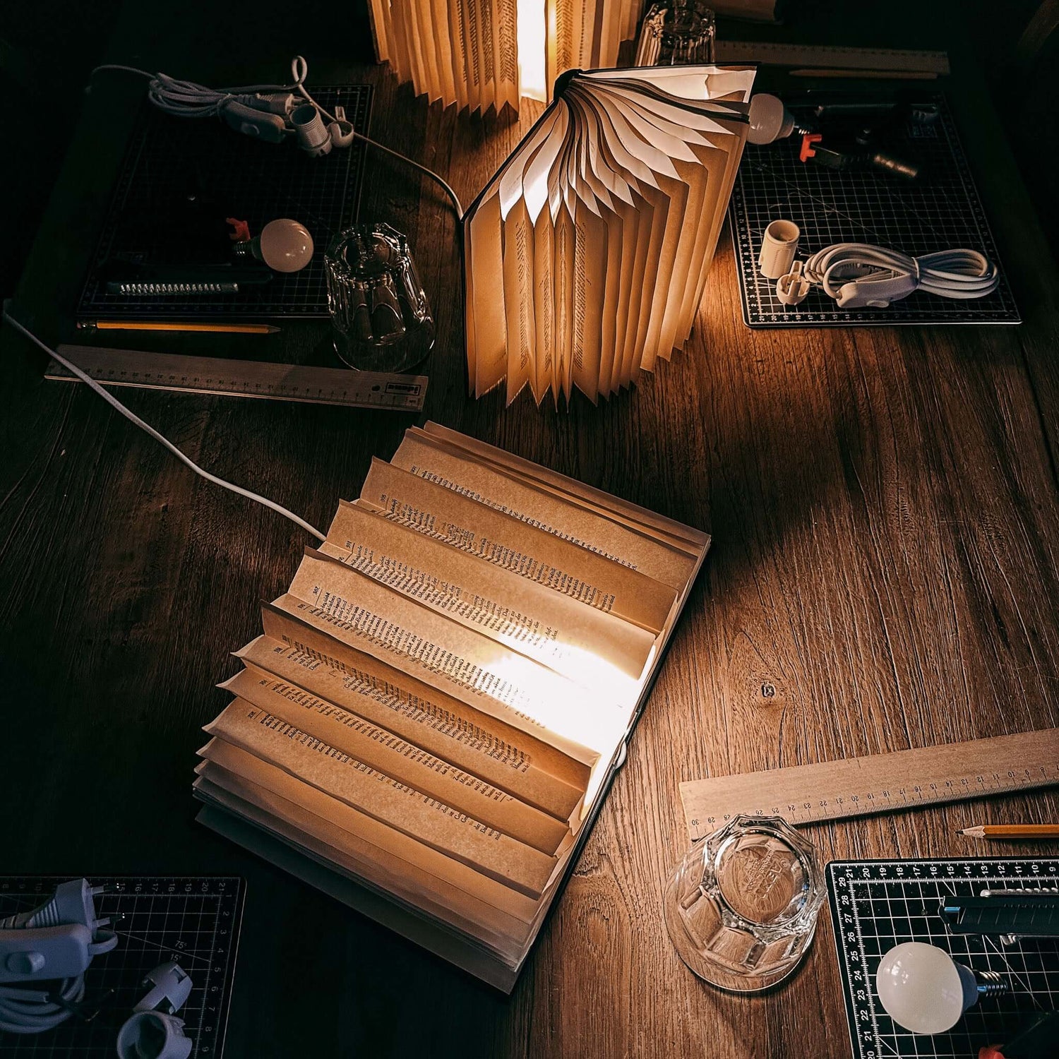 Offenes leuchtendes Buch auf Tisch mit Werkzeugen und Materialien – upcycling buchlampe, diy lampe, buch kunst. Auch für Firmenevents.