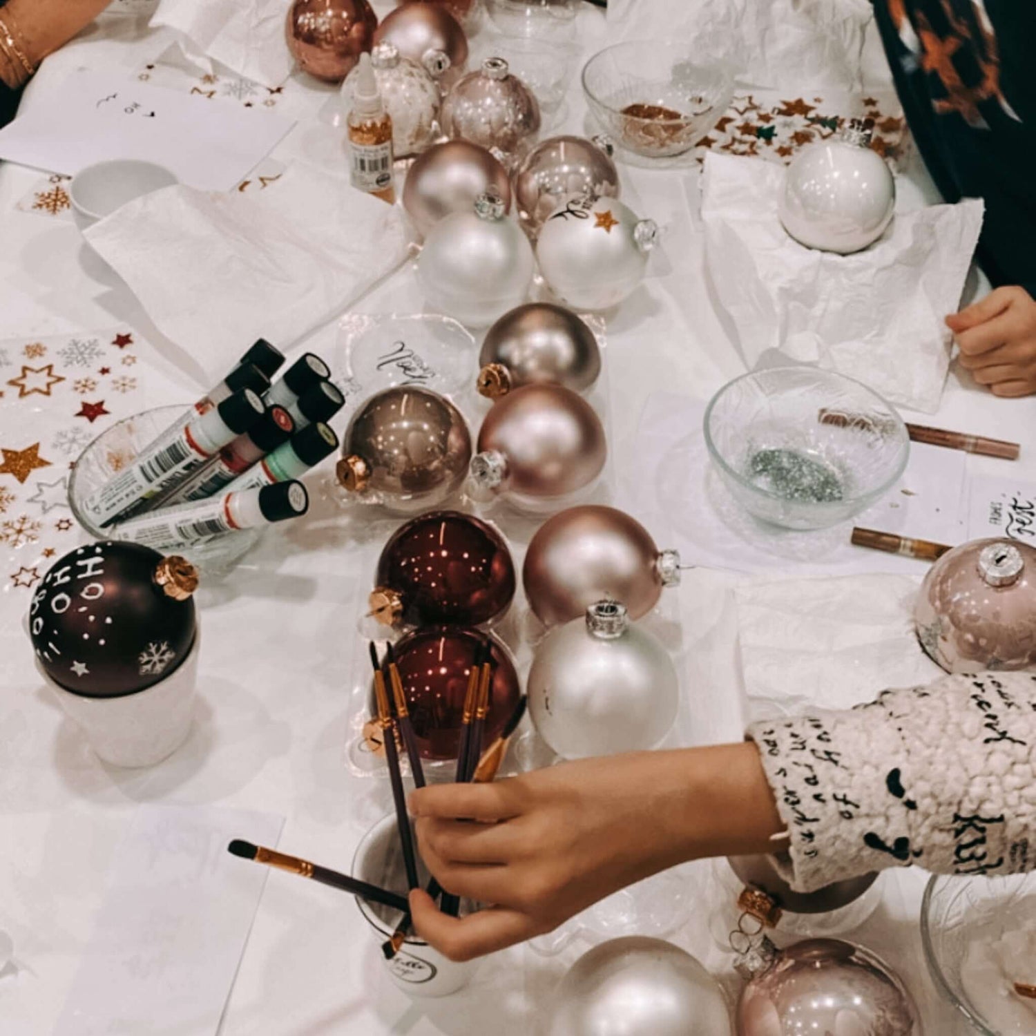 Tisch mit vielen Kugeln, Stiften und Pinseln – Teilnehmer greifen nach Materialien.