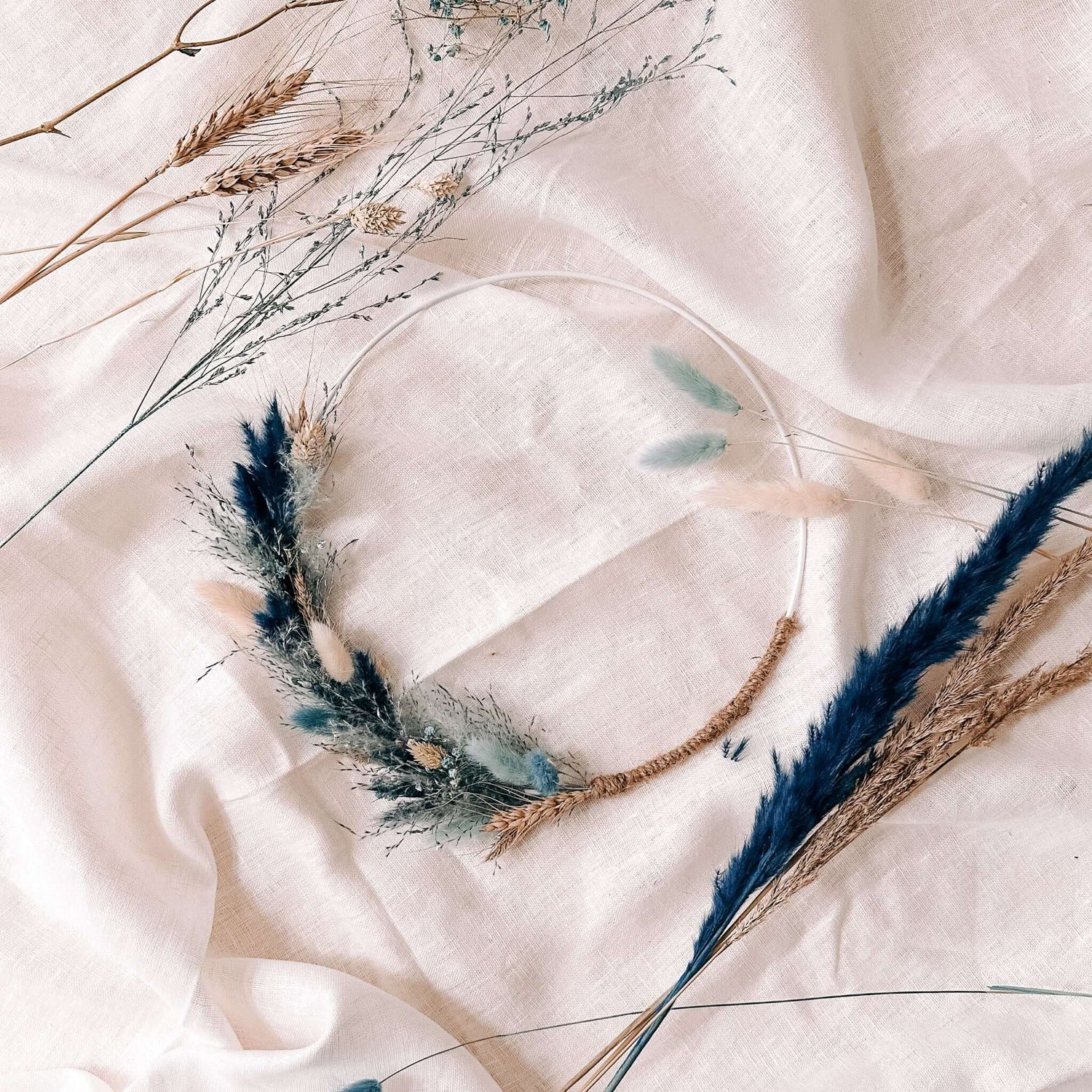Fertiger Trockenblumen Ring „Eisblume“ in Blautönen auf weißem Tuch – stilvolle DIY Wanddeko.