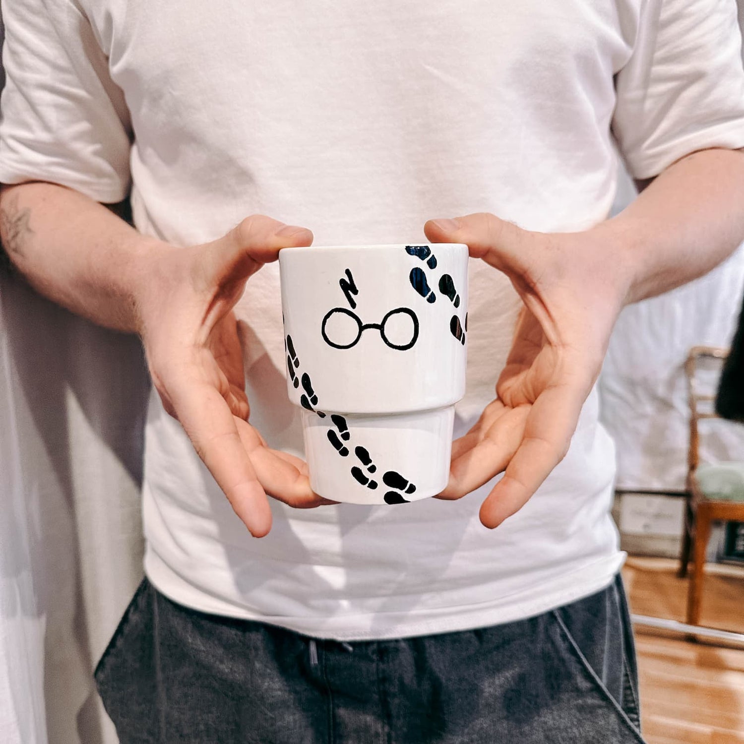 Zwei Hände halten handbemalten Becher im Harry Potter Design beim Tassen bemalen Workshop von GRIMMS GARTEN Berlin