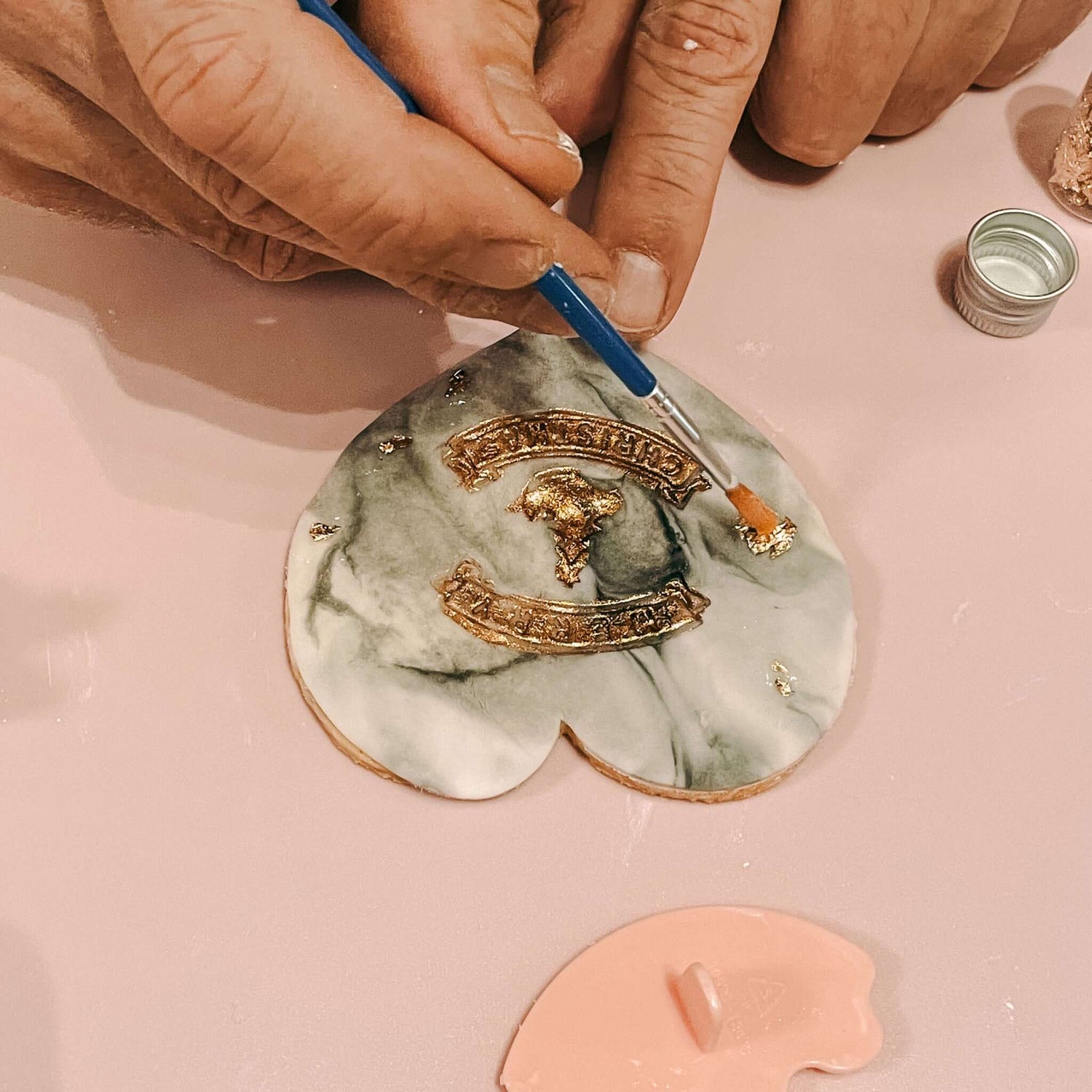 Pinsel trägt goldene Akzente auf graugrünen fondant keks in Herzform auf – fondant kekse weihnachten ideen.Auch als Firmenevent buchbar.