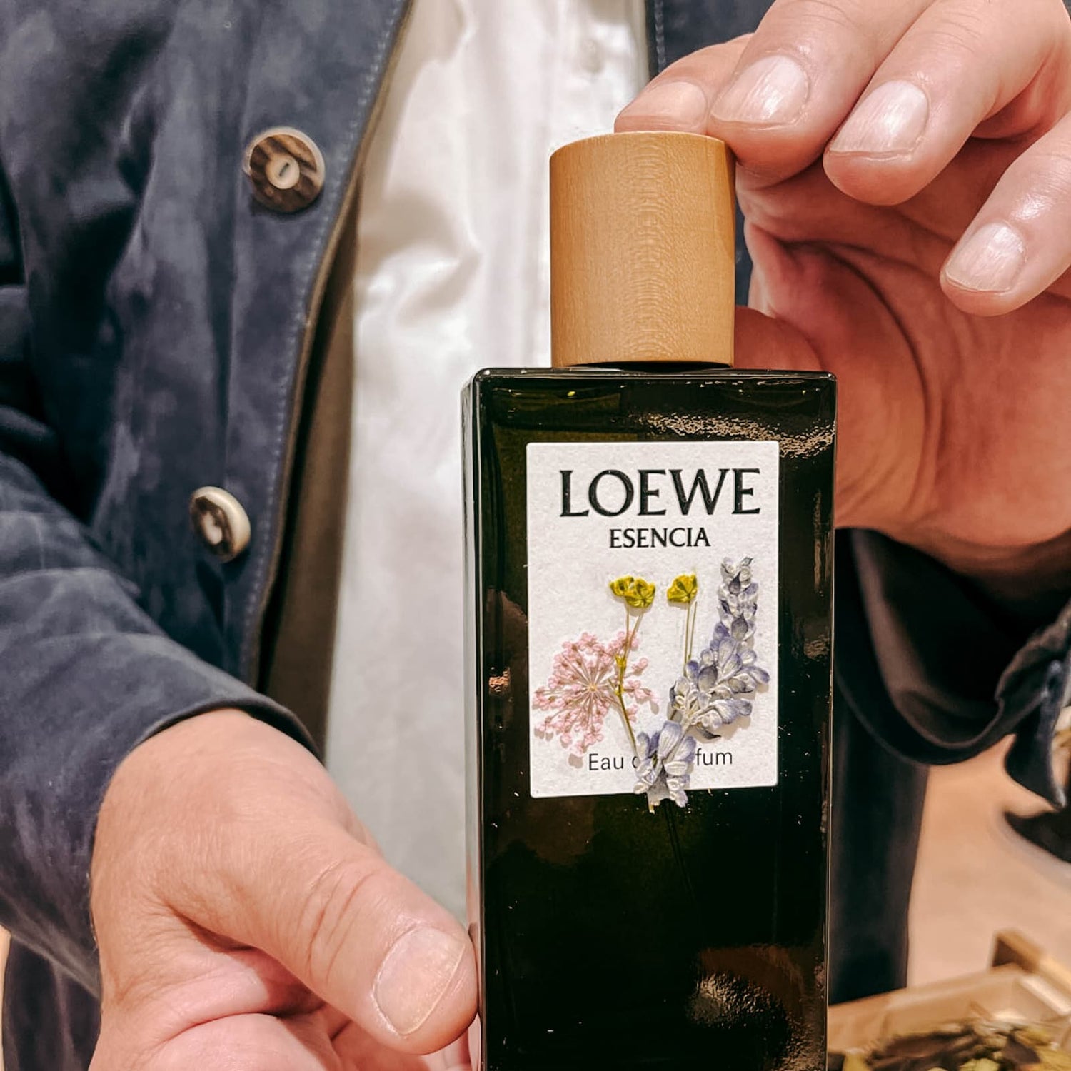 Hände halten dunkelgrünes Parfum mit pastellfarbenen Trockenblumen im DIY Workshop von GRIMMS GARTEN Berlin