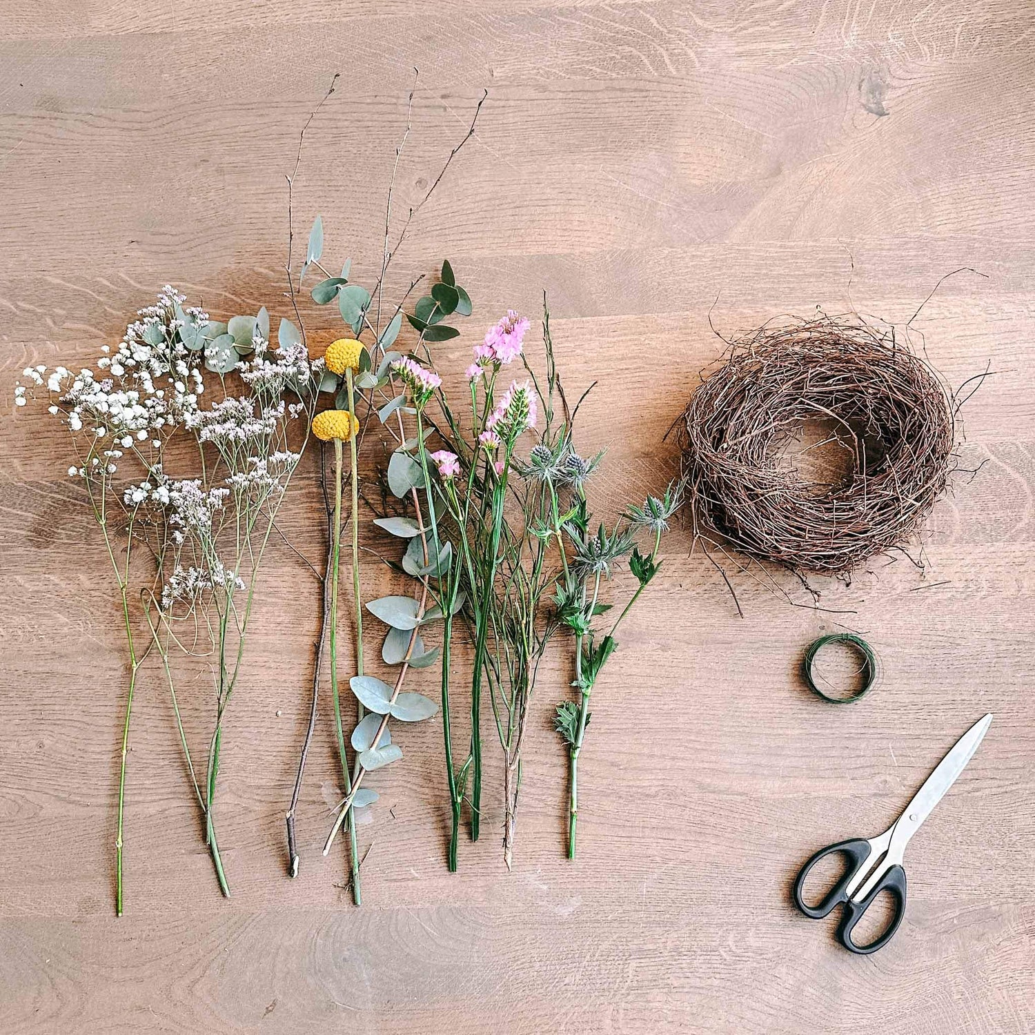 Blumen, Schere und Draht auf Basteltisch – Materialien für DIY Frühlingskranz aus Blumenbox.
