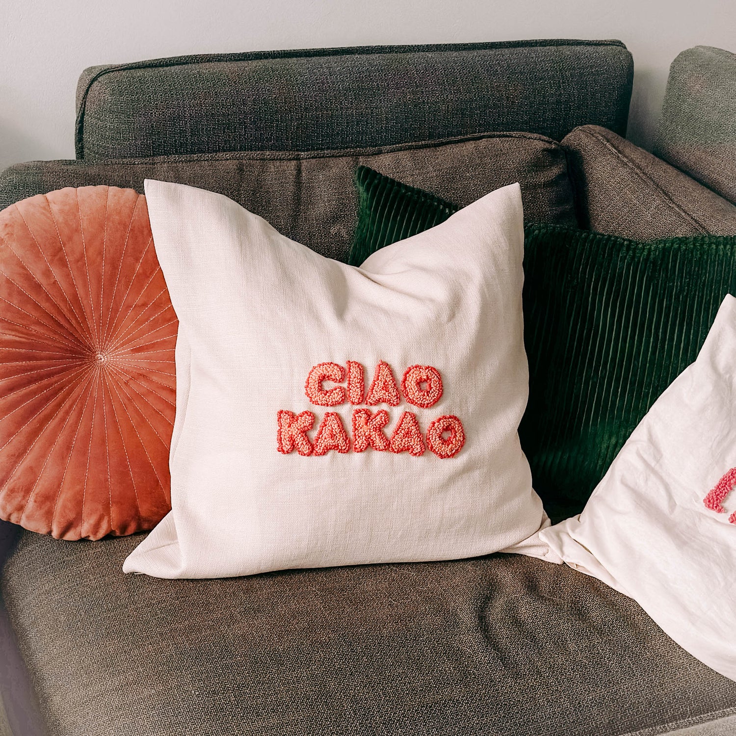 Kissen mit „Ciao Kakao“ auf Sofa, andere Kissen im Hintergrund – textiler Punch-Needle Workshop.