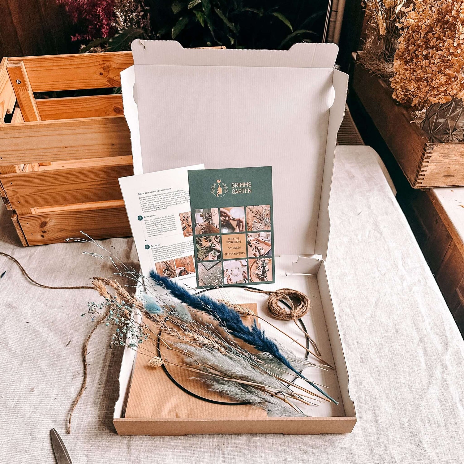 Offene DIY Box mit allen Materialien für Trockenblumenring Eisblume auf Tisch ausgebreitet.