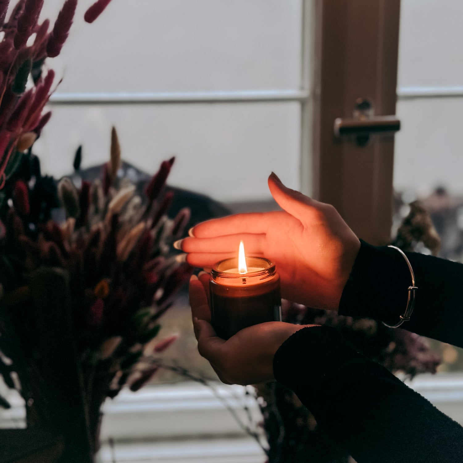 Zwei Hände halten brennende vegane Duftkerze – handgemachte Kerze aus Rapswachs.