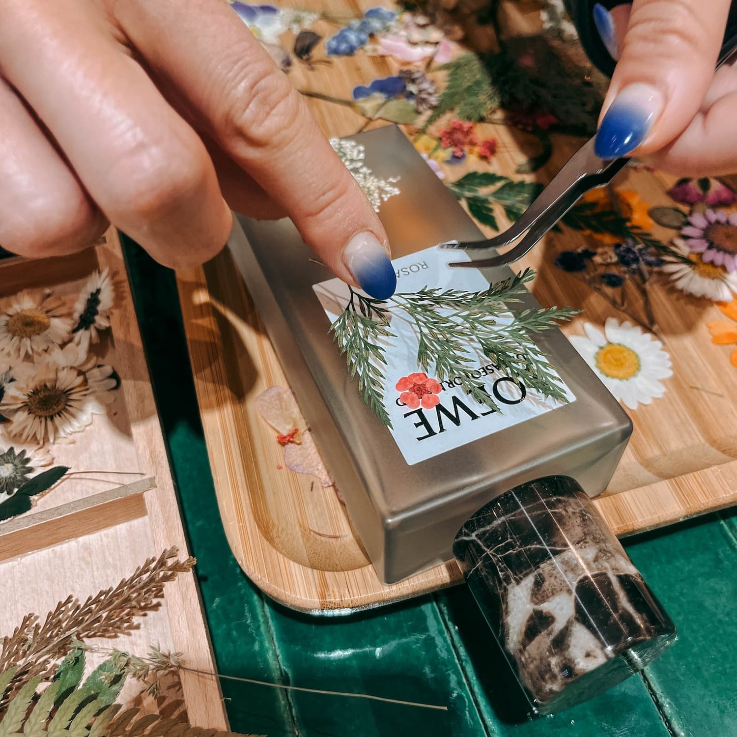 Hände kleben Trockenblume auf Parfum Flakon im kreativen DIY Workshop von GRIMMS GARTEN Berlin
