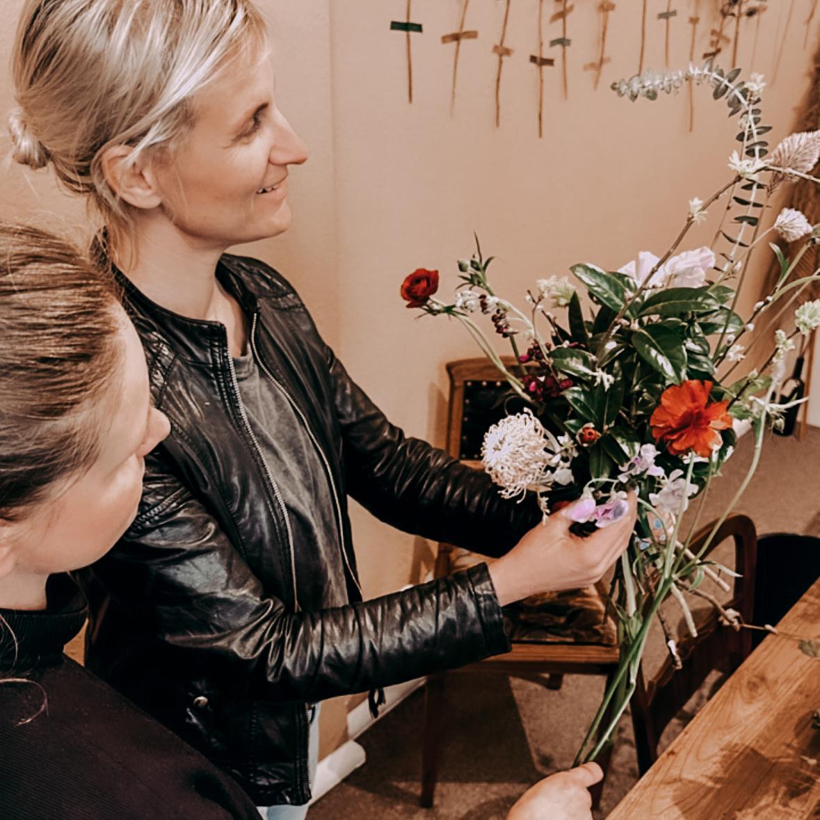 Frau zeigt ihrer Begleitung ihren Blumenstrauß – DIY Flower Bouquet Workshop, Teamevent buchbar.
