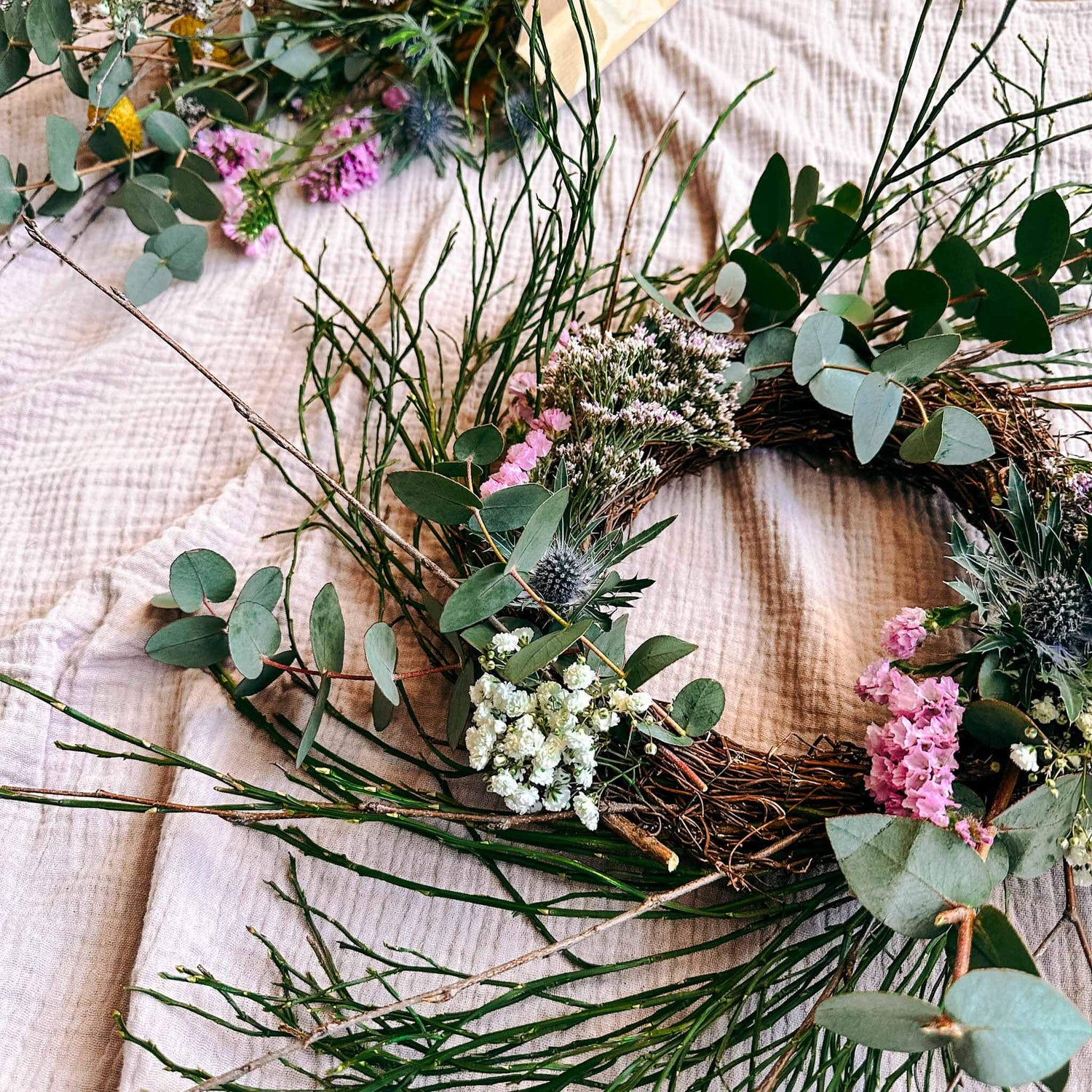 Frühlingskranz mit bunten Blumen und Eukalyptus auf weißem Tuch – DIY Deko zum Selbermachen.