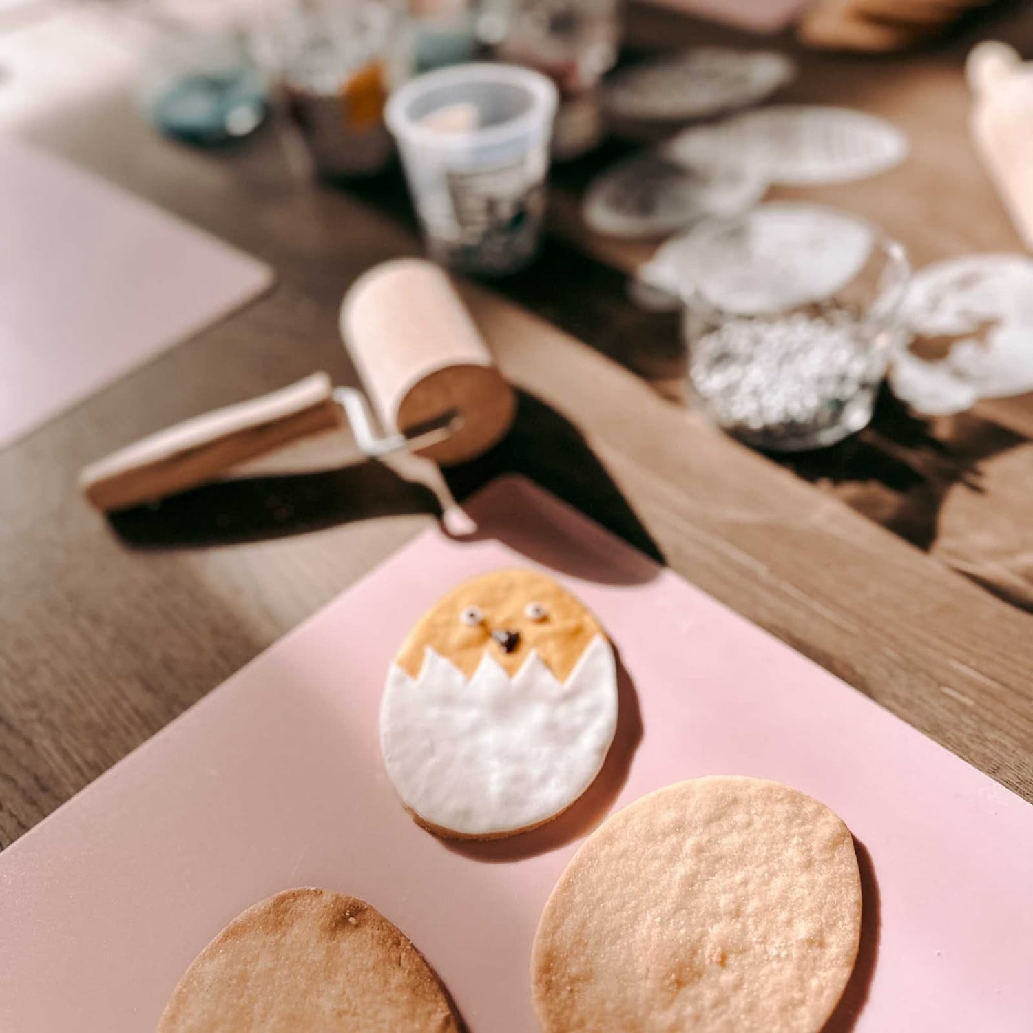 Küken in Eierschale als dekorierter Osterkeks neben zwei unfertigen Keksen und Fondantrolle auf dem Tisch beim Osterkekse Workshop von GRIMMS GARTEN in Berlin