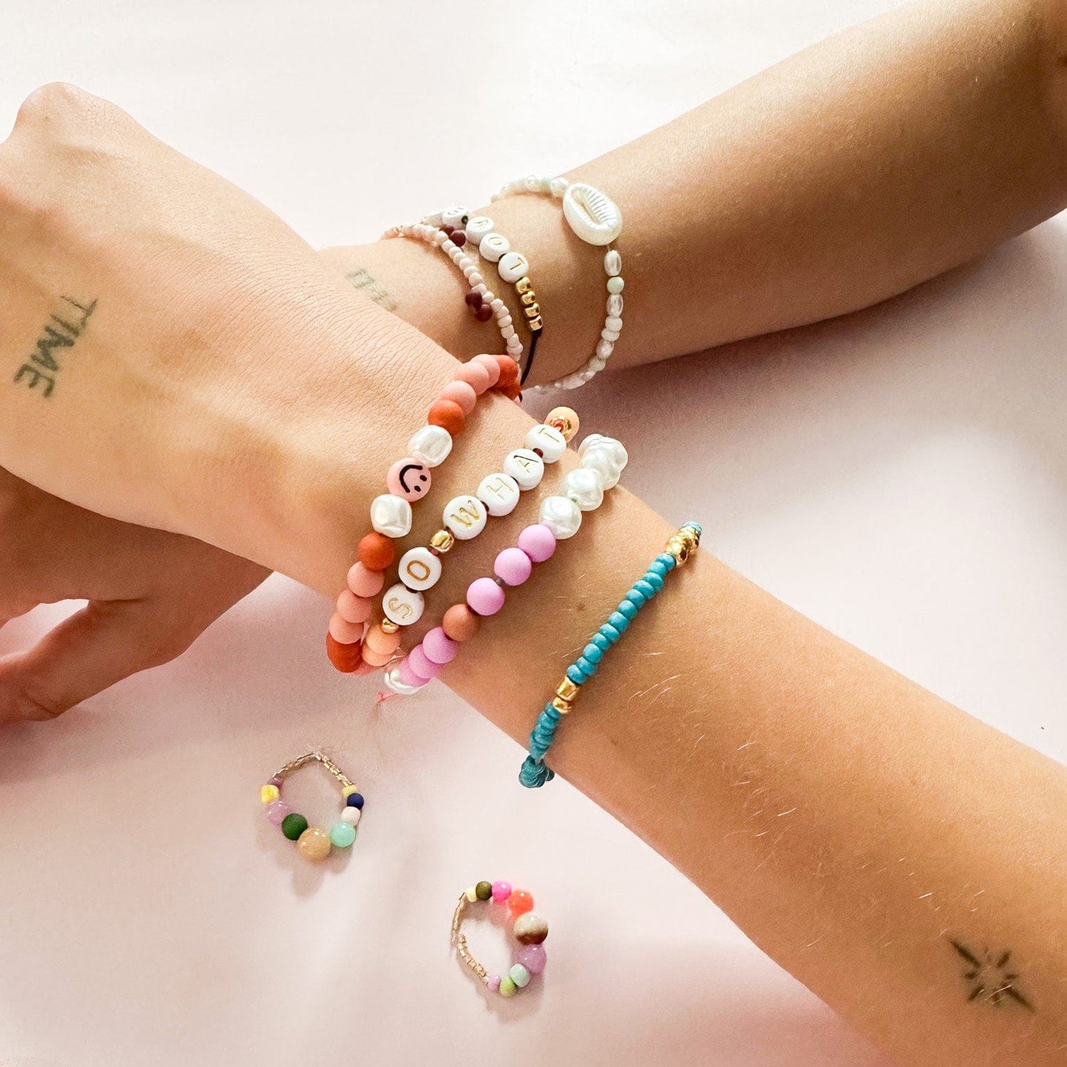 Zwei Handgelenke mit verschiedenen Armbändern in verschiedenen Farben- DIY Perlenarmband workshop.