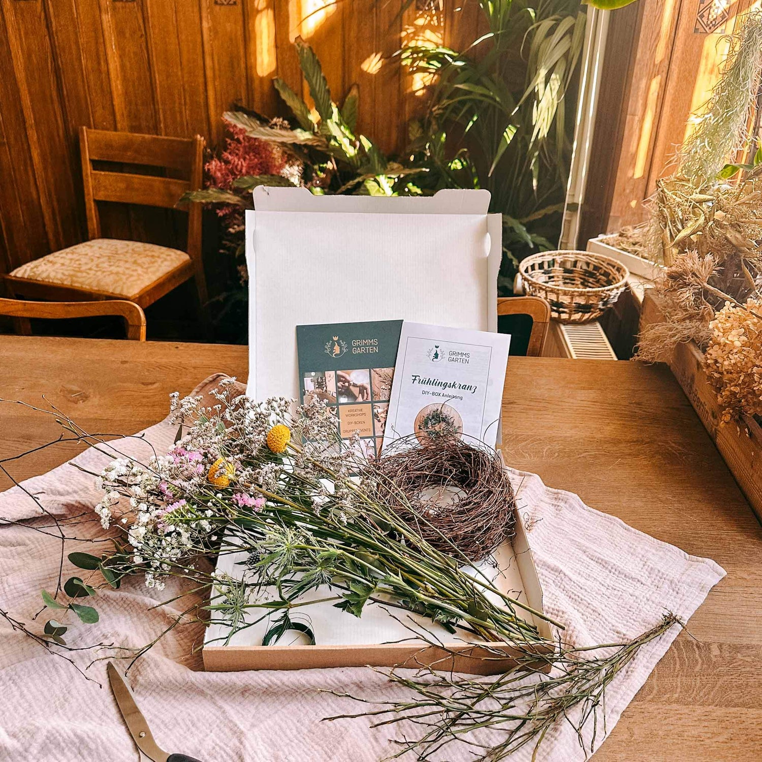 Offene DIY Box Frühlingskranz mit frischen Blumen, Zweigen und Bastelanleitung auf Tisch.