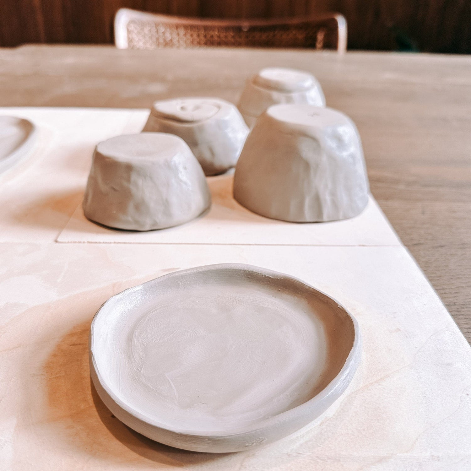 Runder Ton-Untersetzer im Vordergrund, fertige Schüsseln unscharf im Hintergrund – Keramik Workshop Berlin Ergebnisse