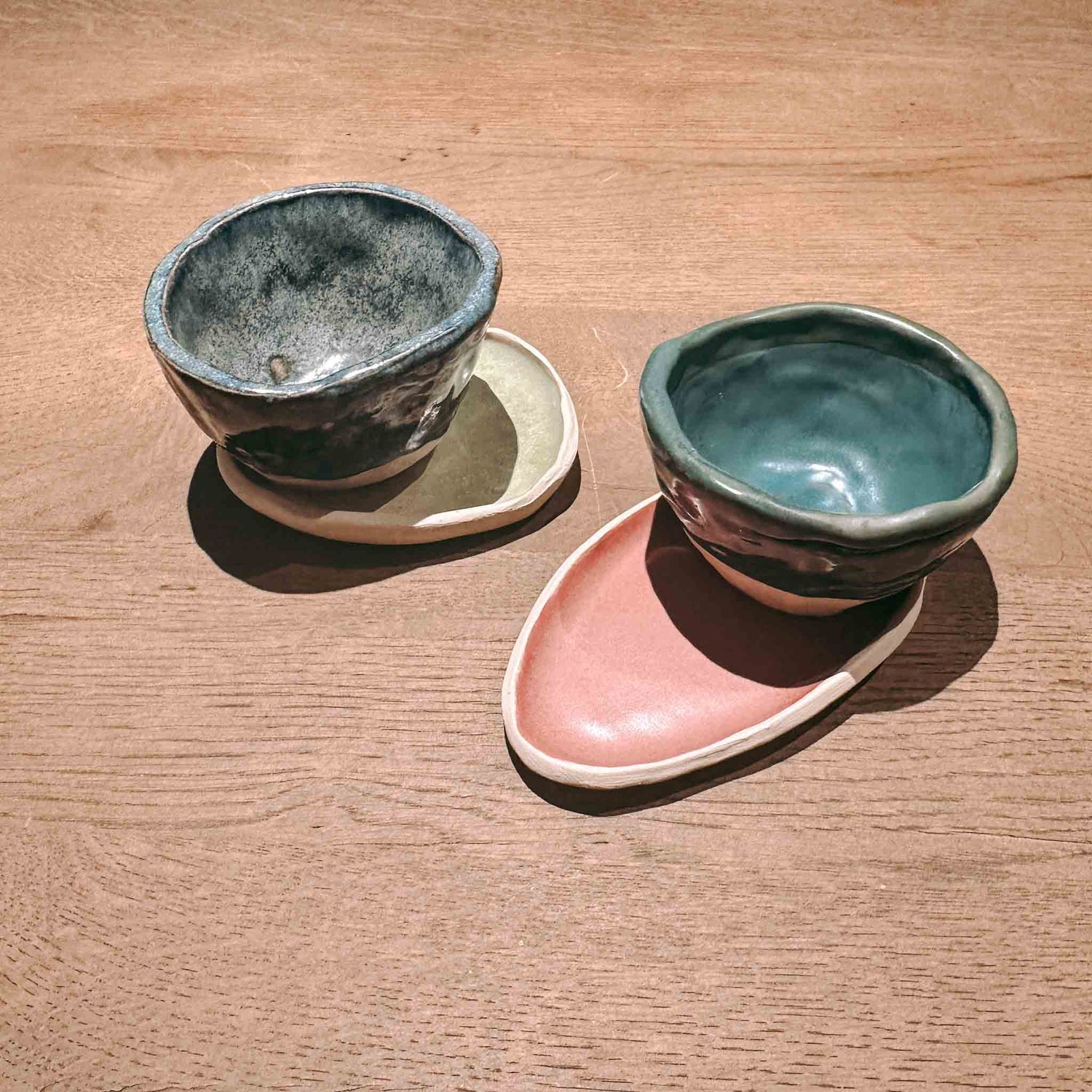 Zwei handgefertigte Kaffeetassen mit Untertassen in verschiedenen Farben auf einem Tisch.