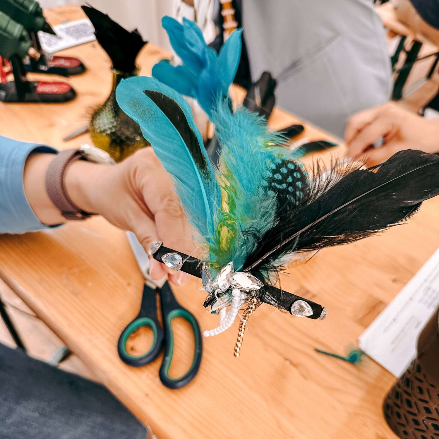 Hand hält fertigen Haarschmuck in Blau und Schwarz – kreatives 20er Jahre Teamevent oder JGA.