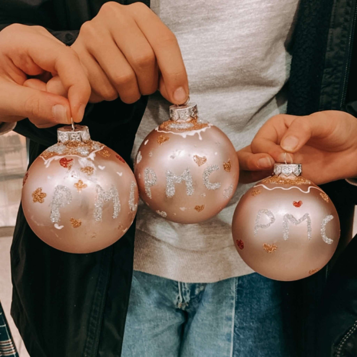 Drei Weihnachtskugeln in Rosa mit Gold- und Silberakzenten hochgehalten – Teamevent Dekoration.