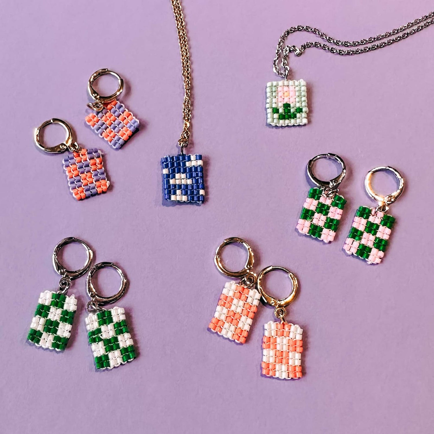 Viele bunte Perlenohrringe mit unterschiedlichen Motiven sowie zwei Halsketten auf lila Hintergrund aus dem DIY Perlenschmuck Workshop von GRIMMS GARTEN, Kreativkurs Berlin