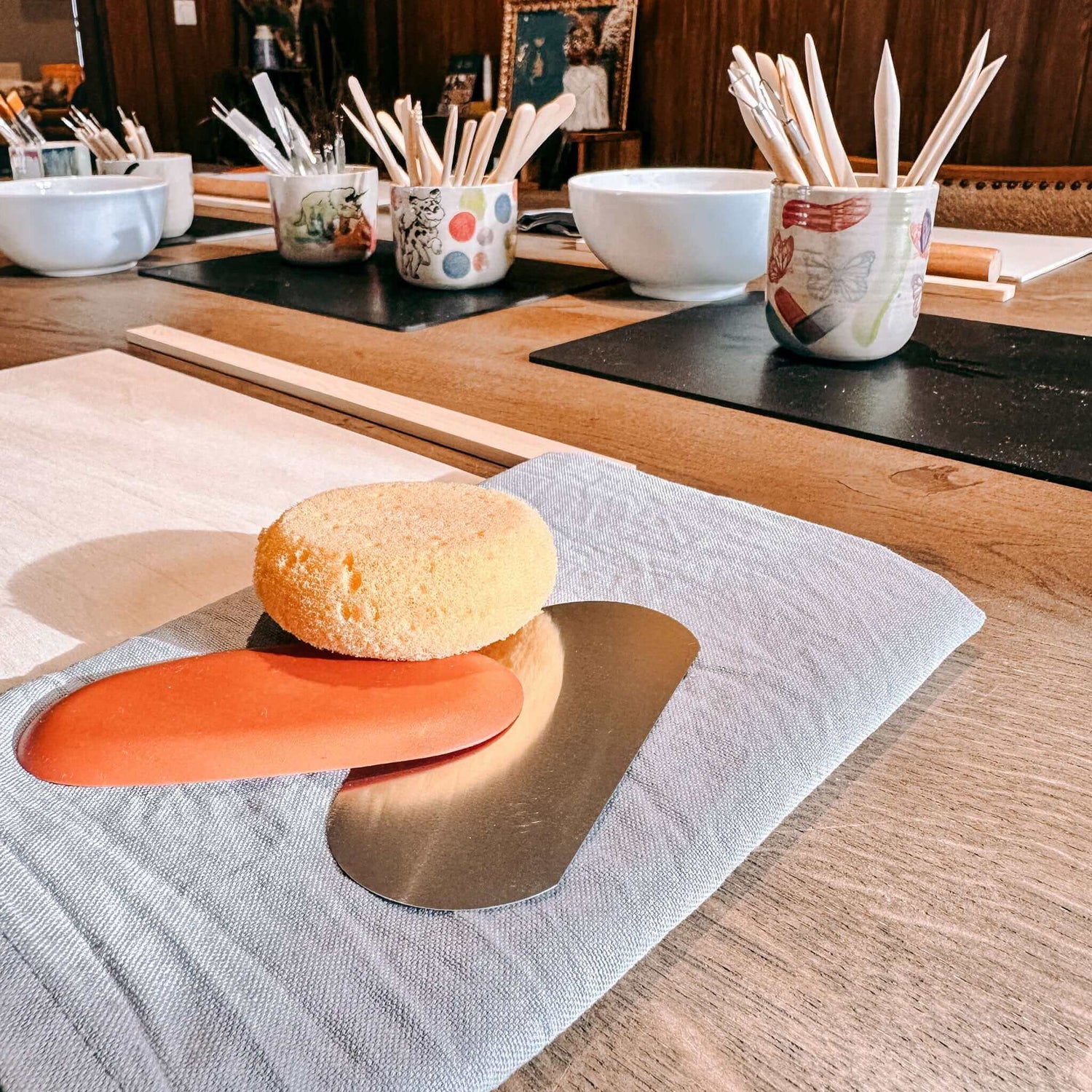 Schwamm, und Töpferwerkzeuge auf Tuch neben Holzplatte – Arbeitsmaterialien im Workshop