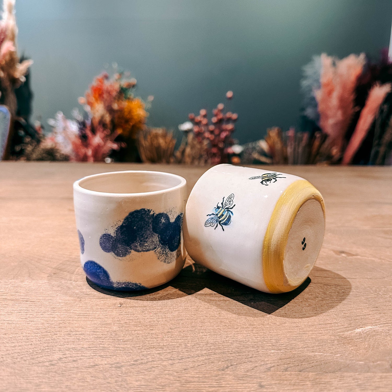 Zwei Keramikbecher auf Tisch – einer steht, einer liegt auf der Seite, DIY Keramik Workshop Berlin, kreativ bemalen