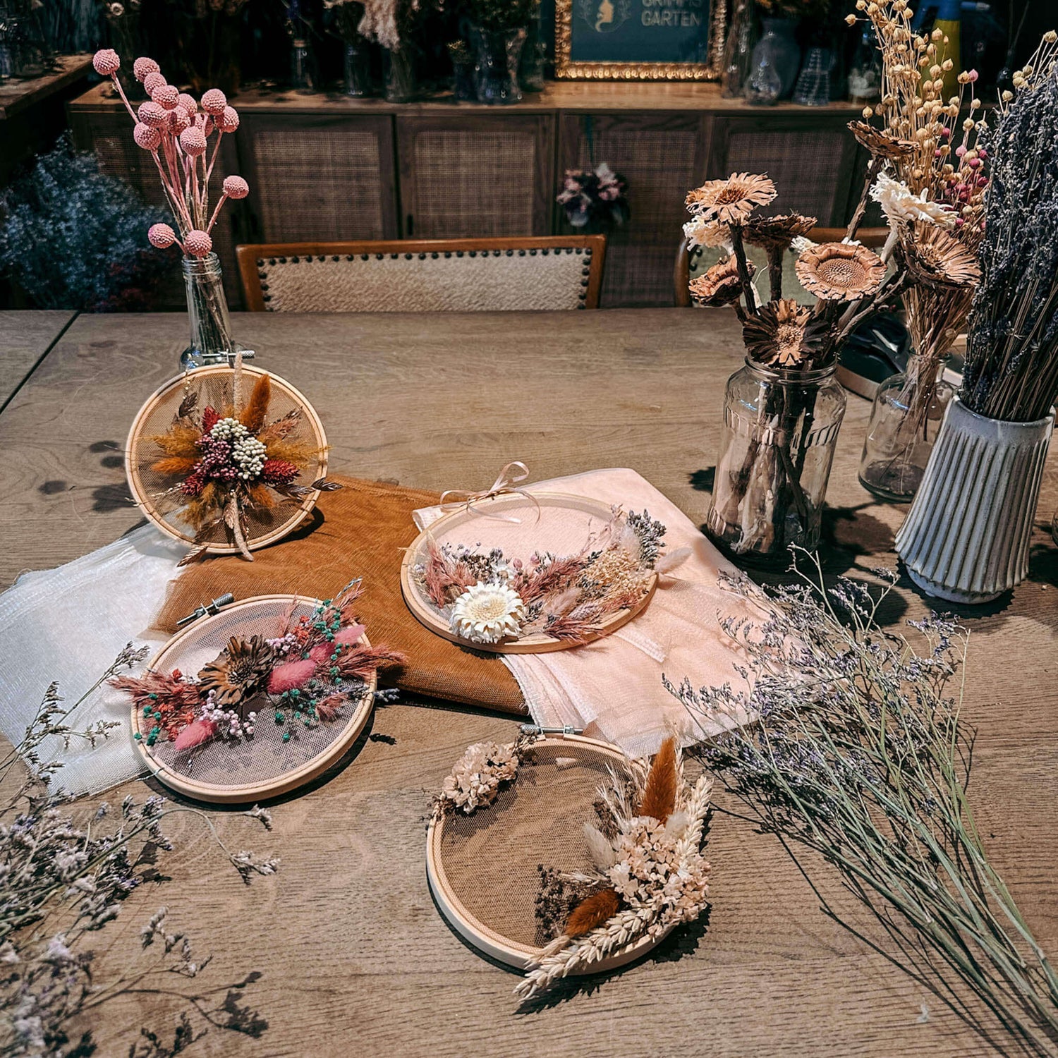 Holztisch mit fertigen Blumenwandbildern, Trockenblumenvasen und Rahmen – DIY Trockenblumen, florales Kunstwerk