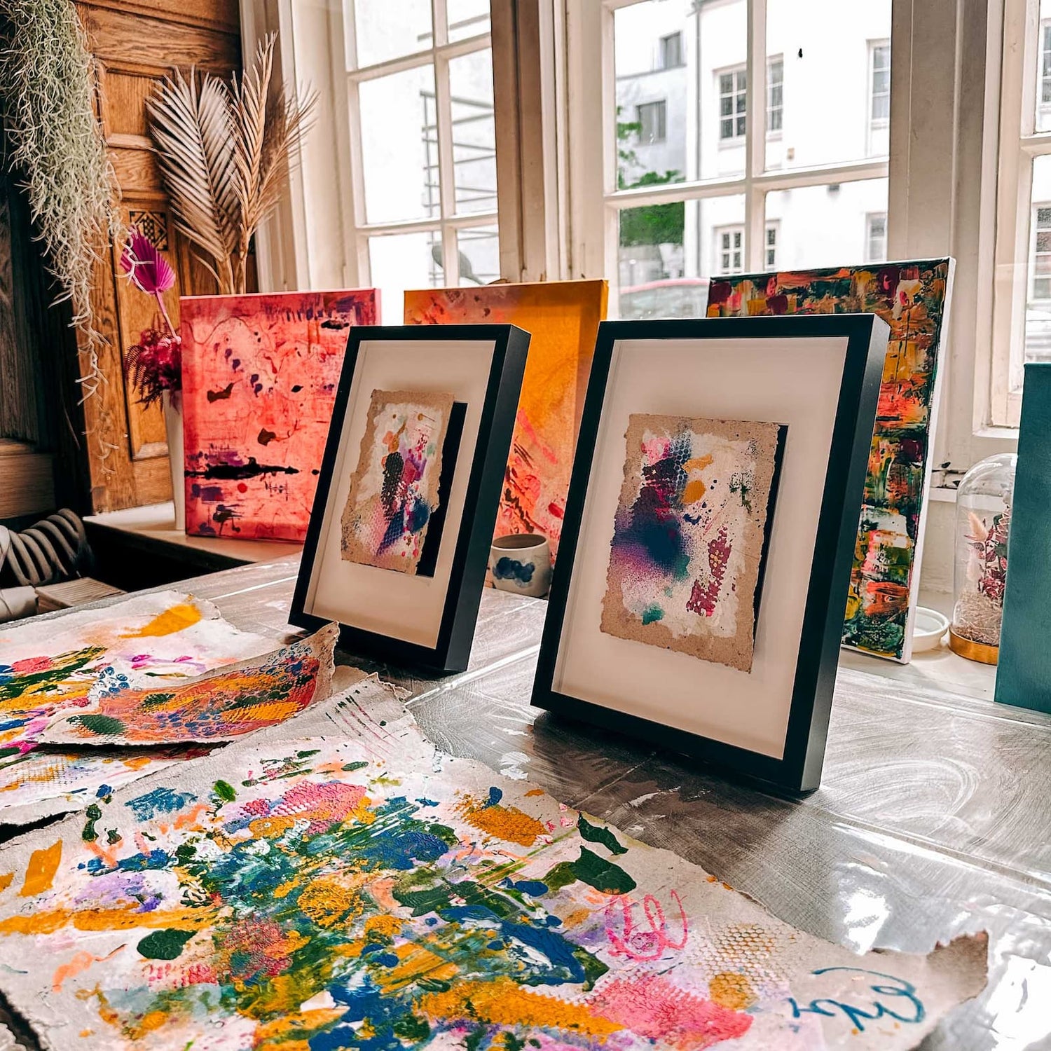 Zwei abstrakt bemalte Malpappen in Bilderrahmen, davor weitere kreative Kunstwerke beim Acryl Workshop von GRIMMS GARTEN Berlin