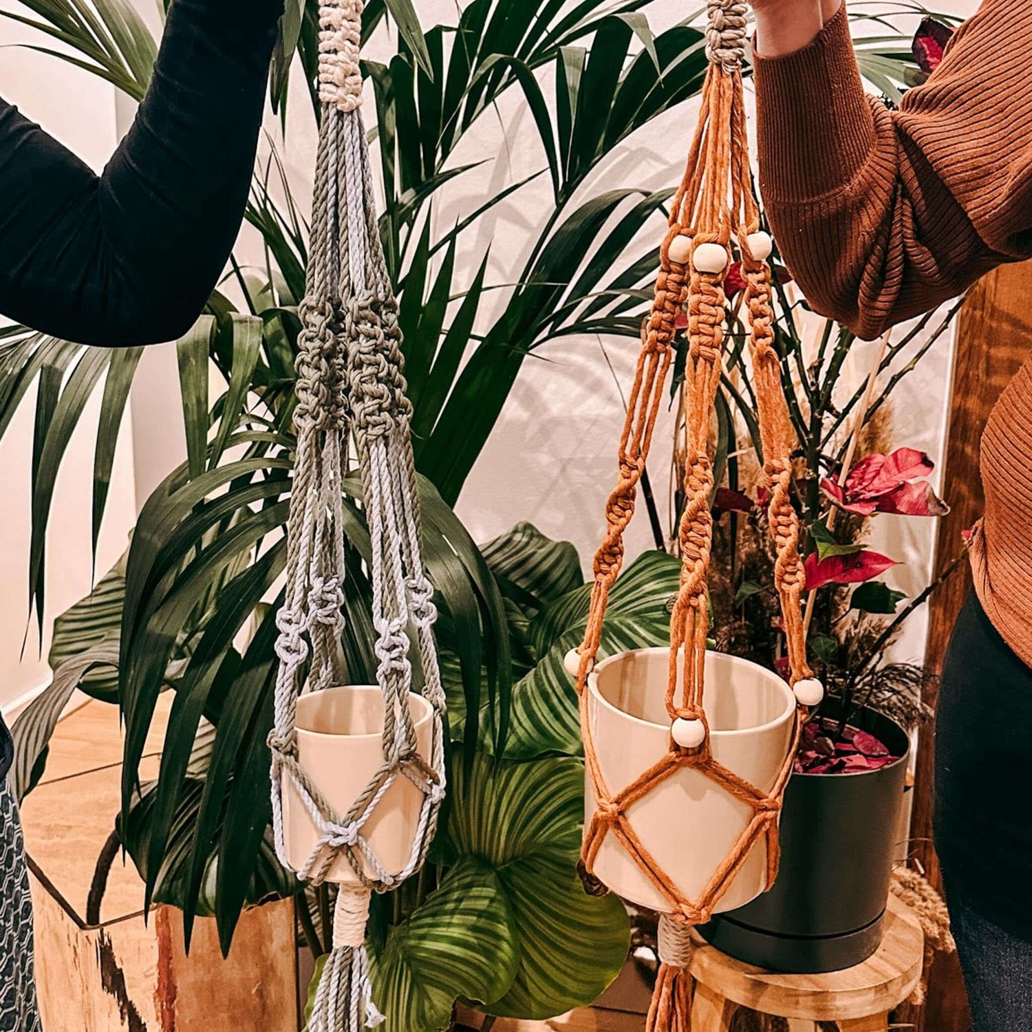 Zwei Personen halten ihre Makrameeampeln hoch – DIY Makramee Workshop, Pflanzenampel, Boho Deko.