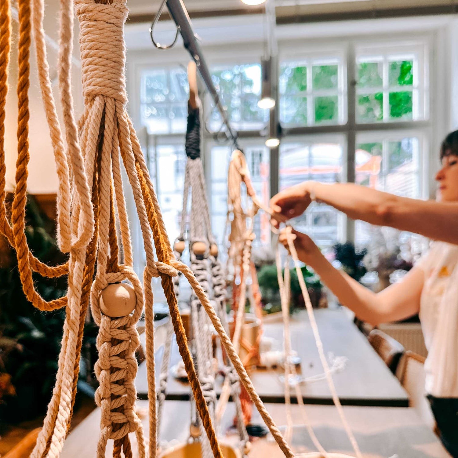 Person hängt verschiedene Makrameeampeln an Stange – DIY Makramee, Blumenampel, Interior Design Workshop.