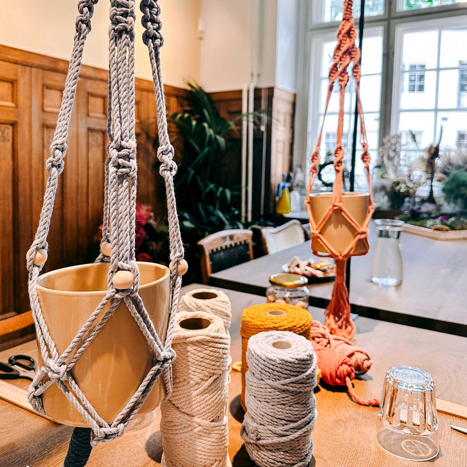 Zwei Makrameeampeln hängen, Makrameekord auf Tisch – DIY Makramee Workshop, Pflanzenhalter, Boho Einrichtung.