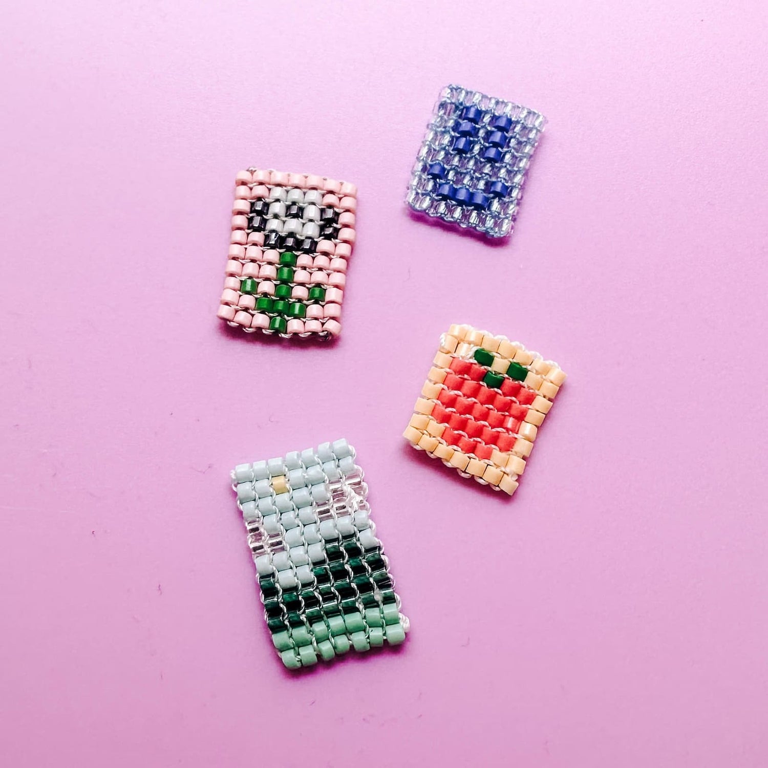 Vier handgemachte Perlenanhänger mit verschiedenen Motiven auf lila Hintergrund aus dem DIY Perlenschmuck Workshop von GRIMMS GARTEN, Kreativkurs in Berlin