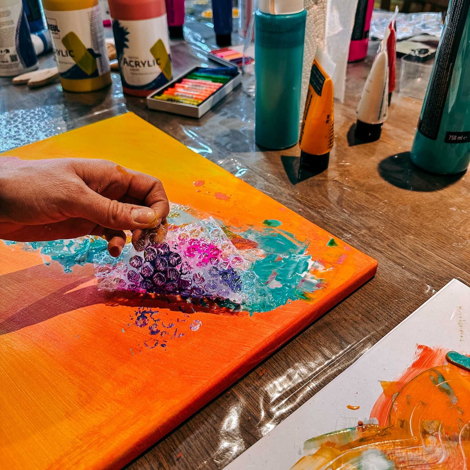 Hand zieht Luftpolsterfolie mit Farbe von bunter Leinwand beim kreativen Abstract Painting Workshop von GRIMMS GARTEN Berlin